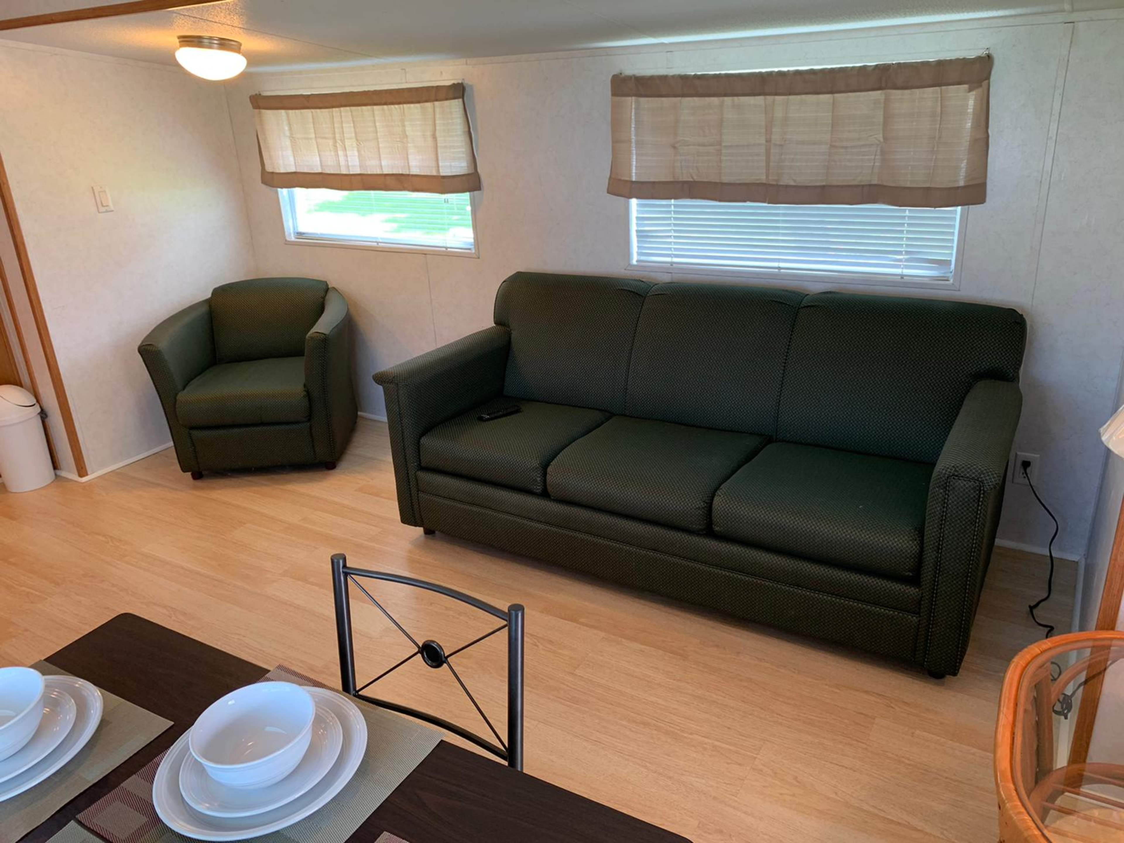 A small living area with a green sofa, a matching armchair, and a dining table set with dishes.