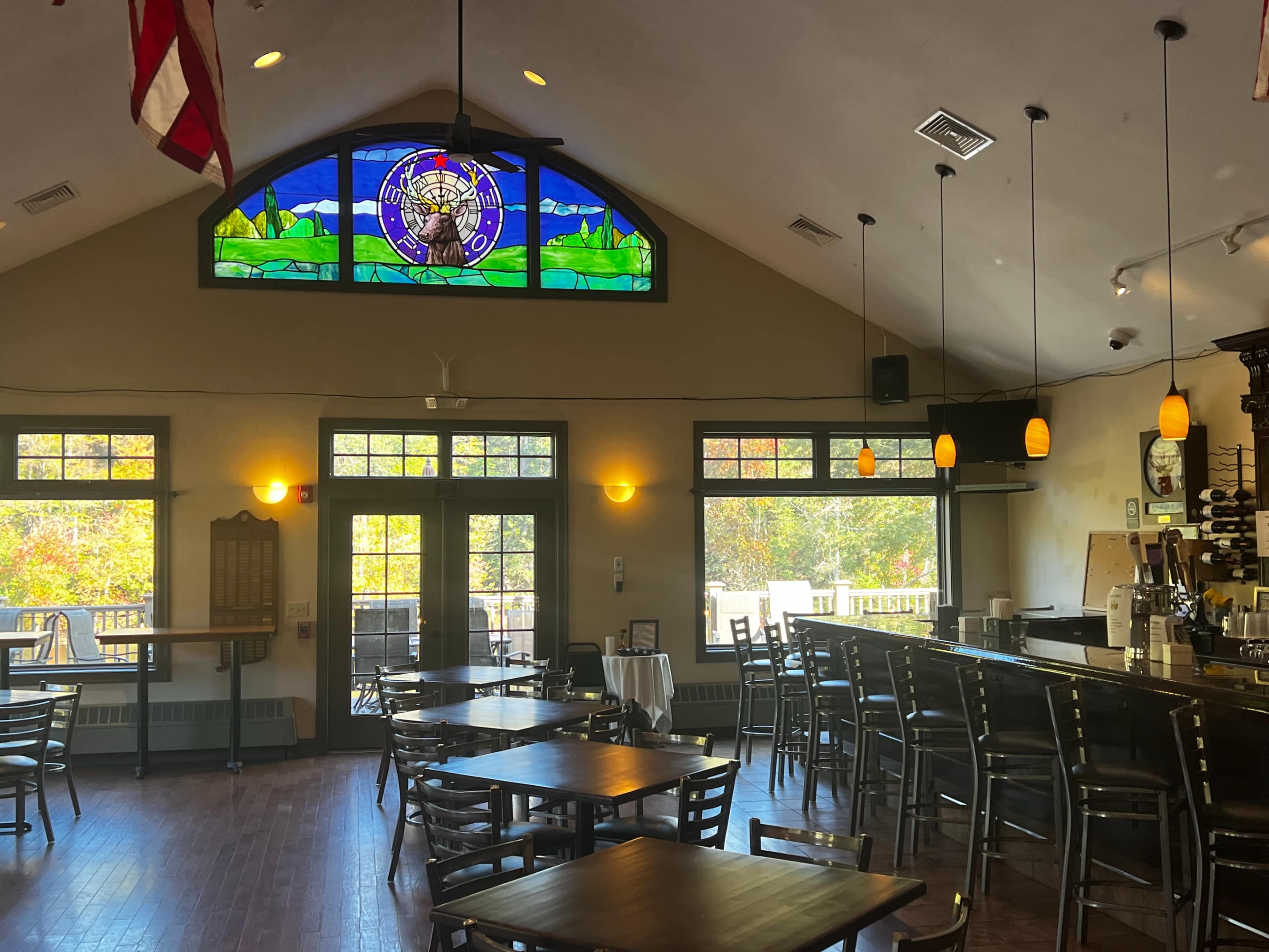 The interior of a restaurant features wooden tables, a bar area, and large windows with a stained glass mural depicting a landscape.