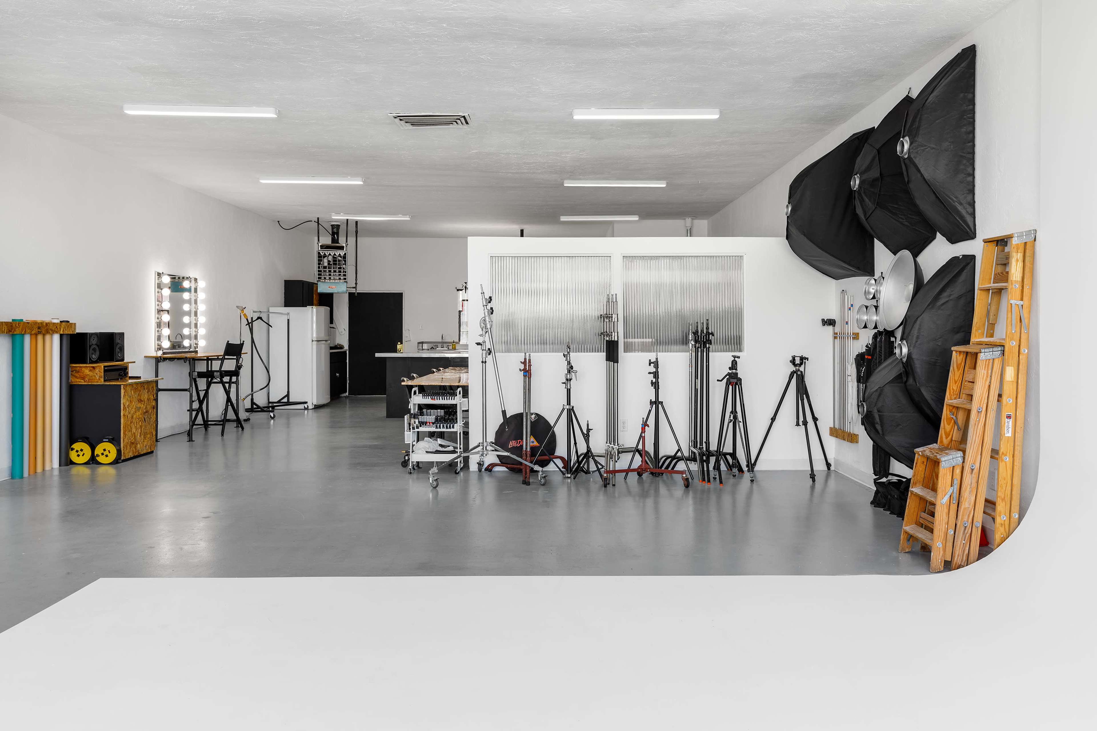 A spacious photography studio featuring various lighting equipment, tripods, and a clean backdrop area.
