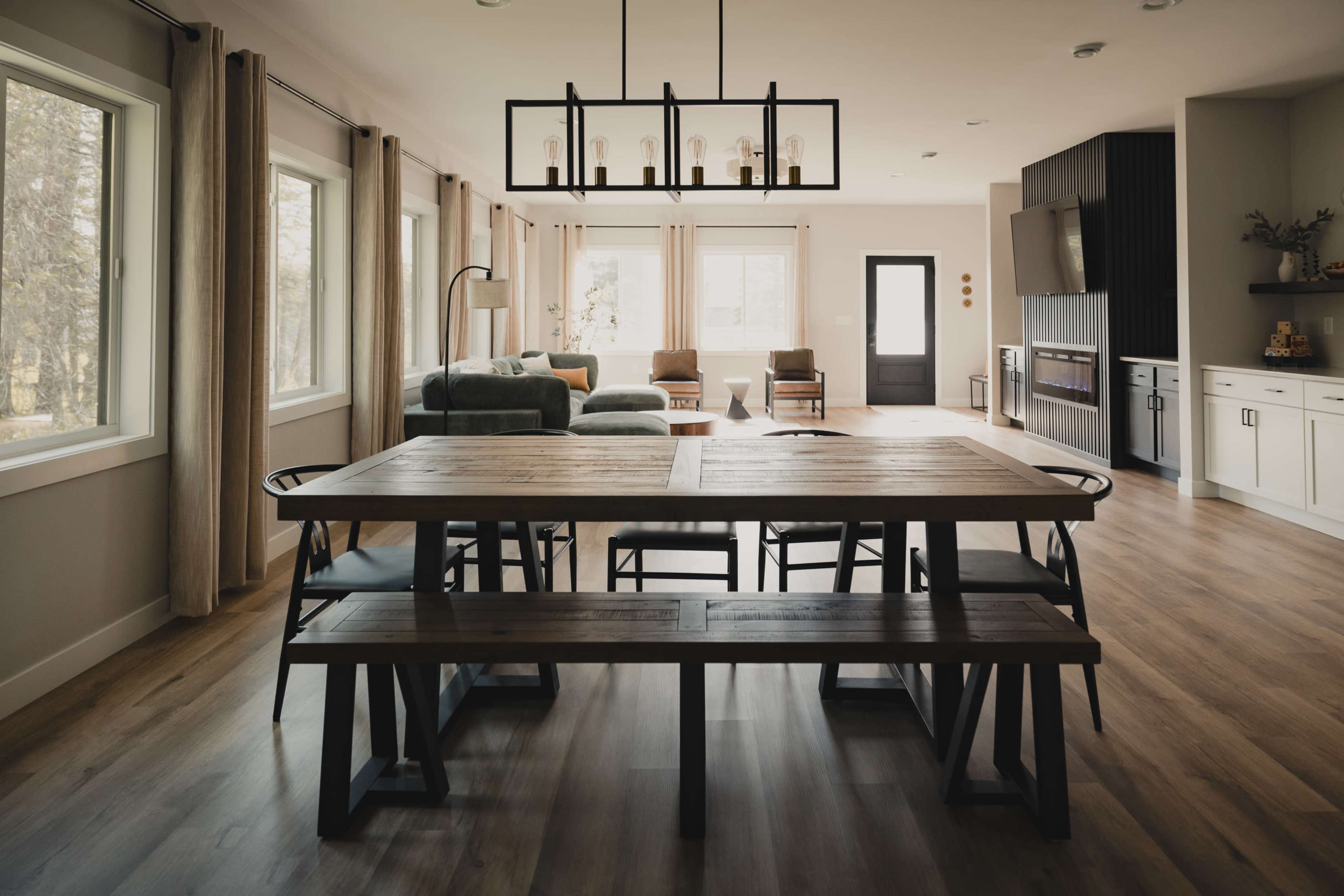 A modern dining area features a wooden table with black metal chairs, set against a backdrop of large windows and a connected living space.