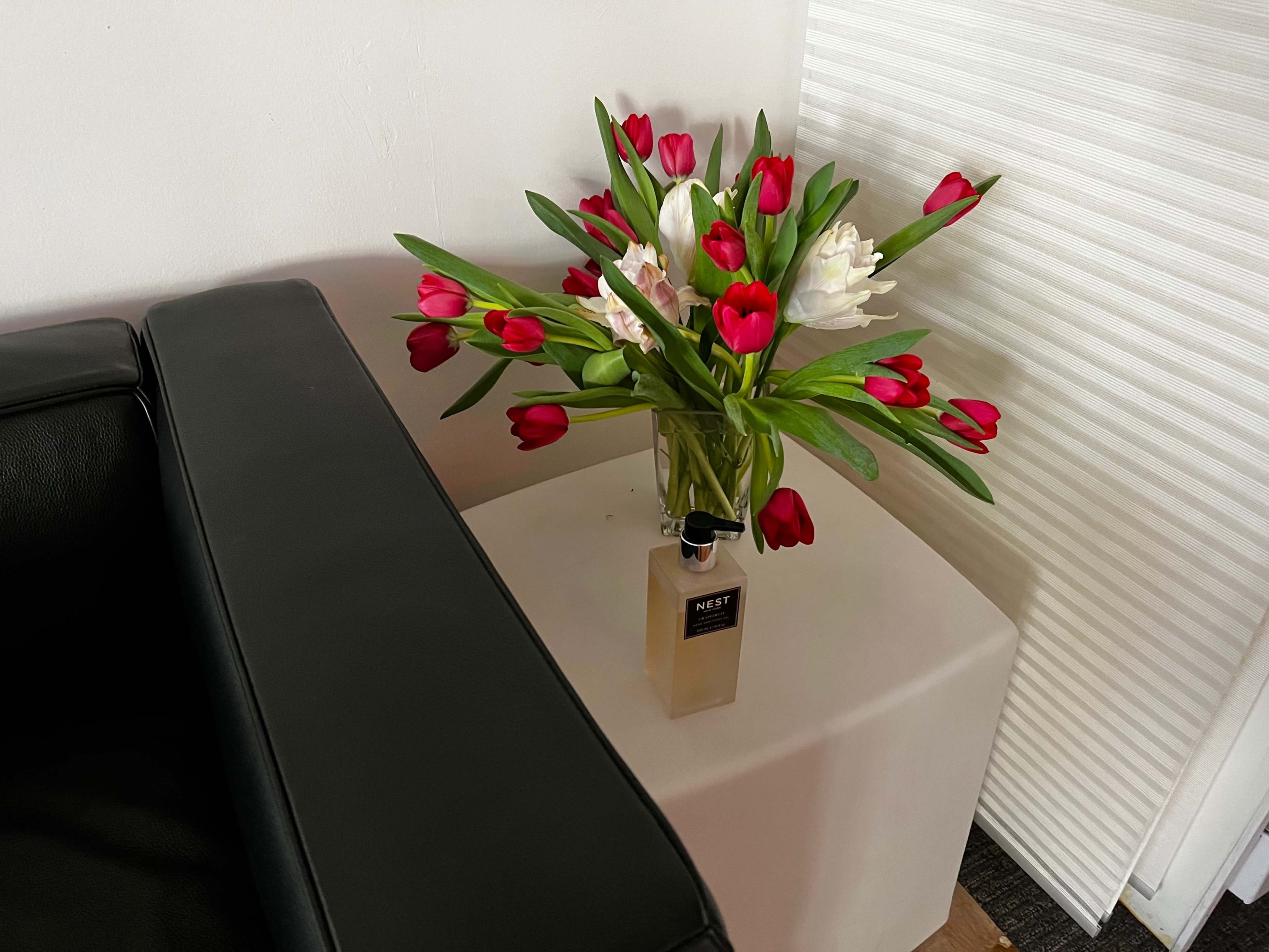 A vase filled with red tulips and white flowers sits on a white table next to a black couch.