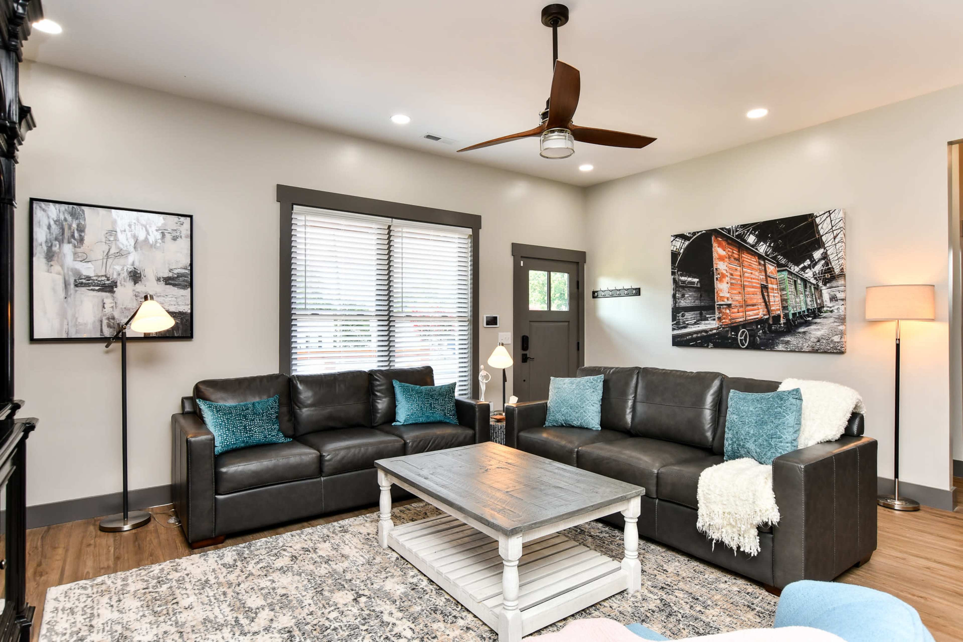 A living room with two black leather sofas, a coffee table, a light blue area rug, and a wall decorated with a black-and-white photograph of a train.