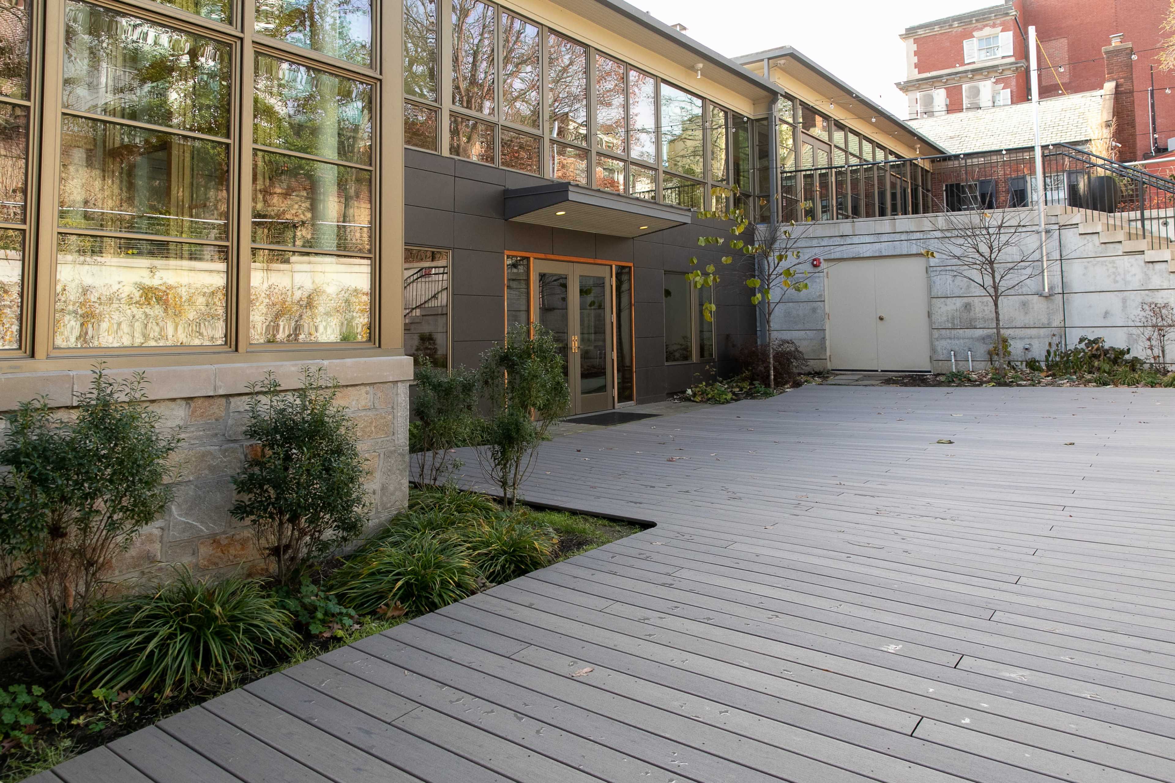 A modern building entrance with large glass windows, surrounded by a wooden deck and landscaped greenery.