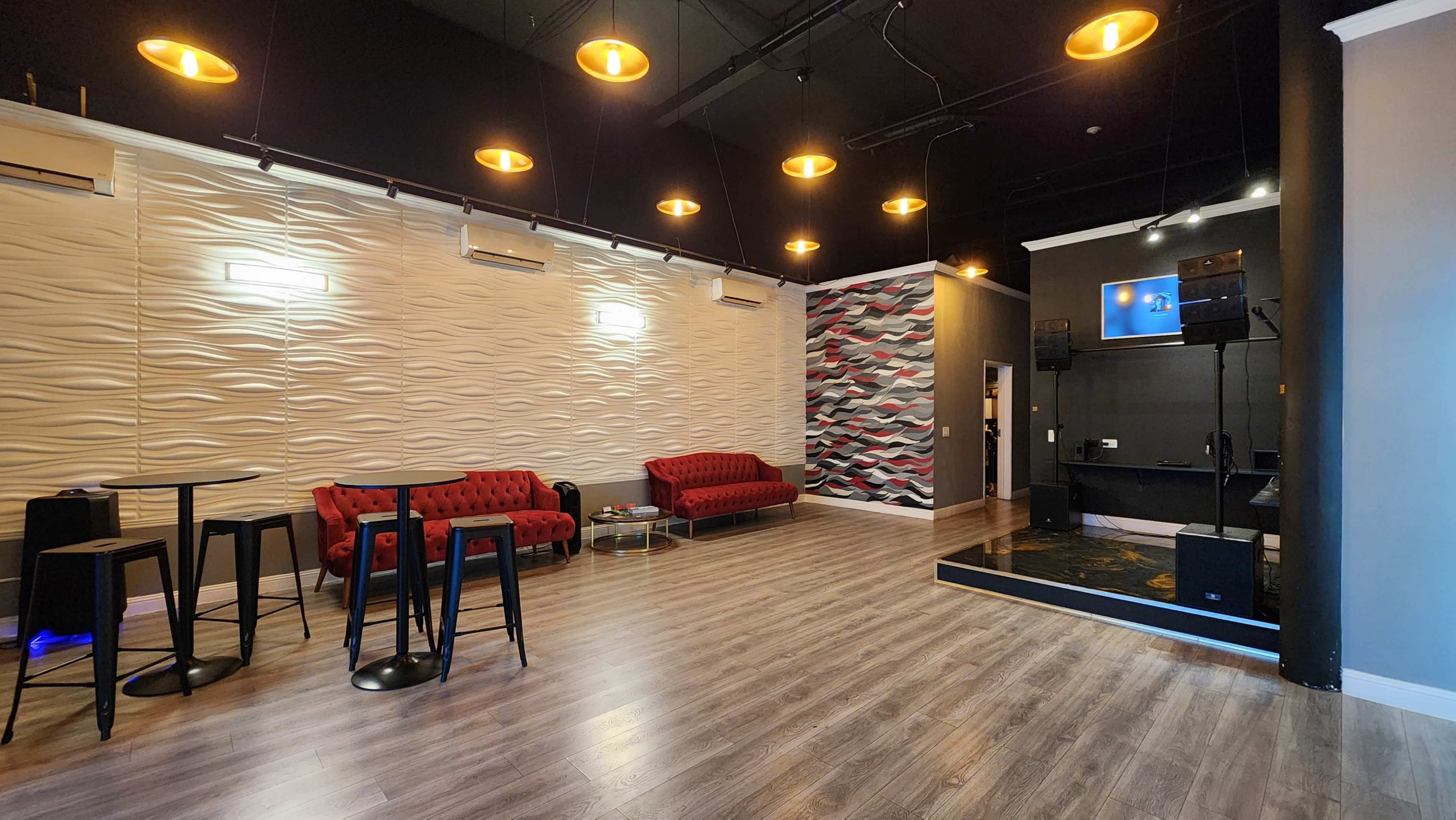 A modern event space with two red sofas, a stage area, and wall-mounted speakers, illuminated by hanging lights.