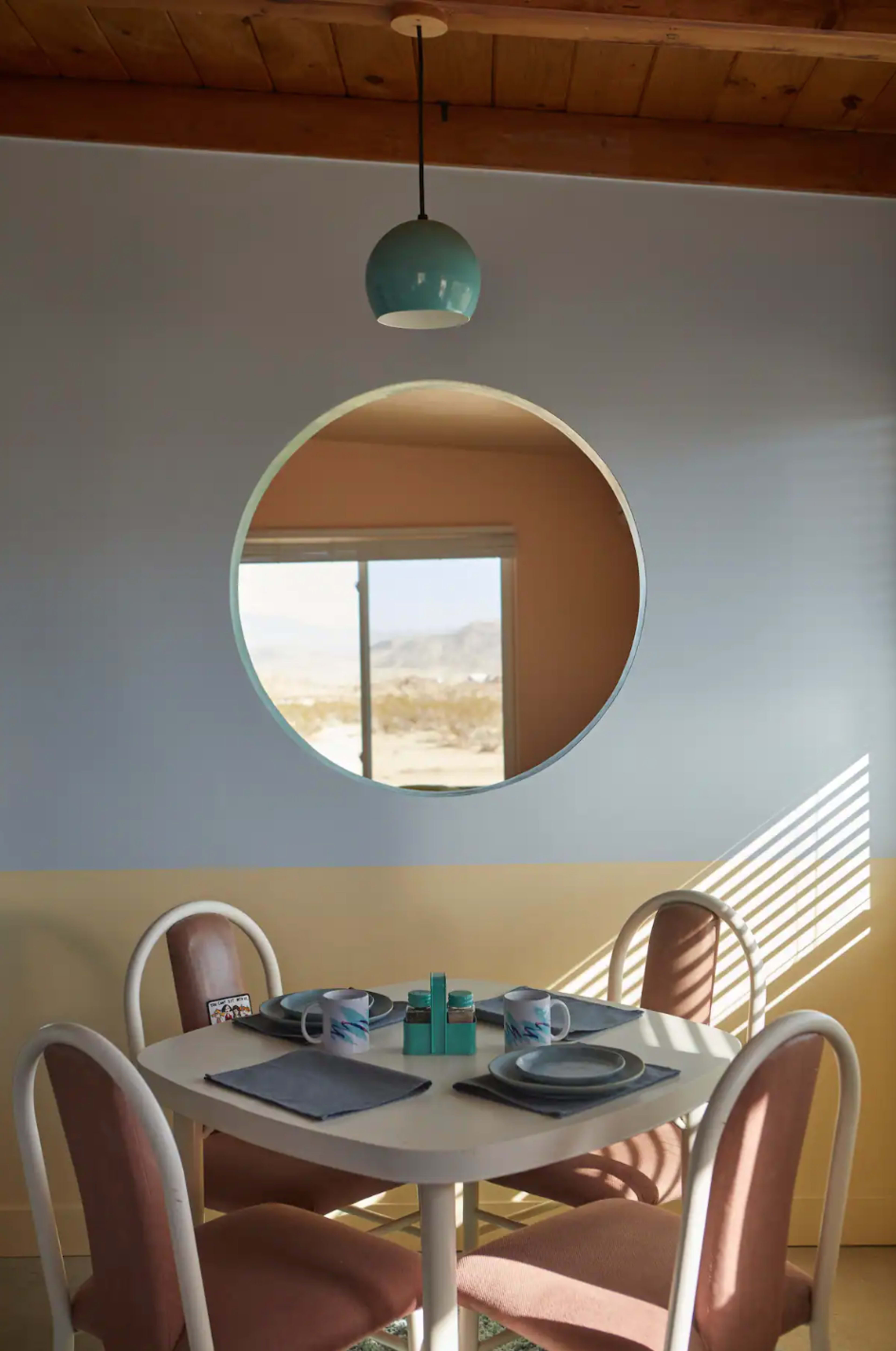 A circular window frames a dining table set with dishes in a room featuring a beige and pastel blue wall.