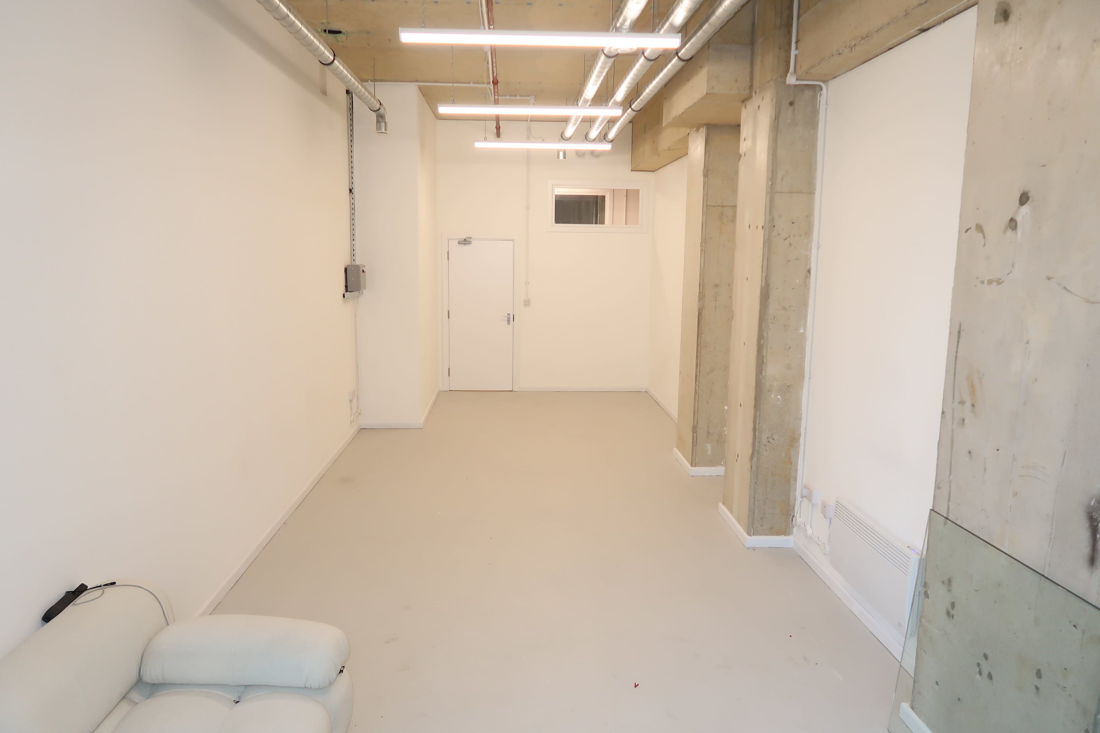 The image shows an empty room with concrete walls, a smooth floor, and a single door at one end.