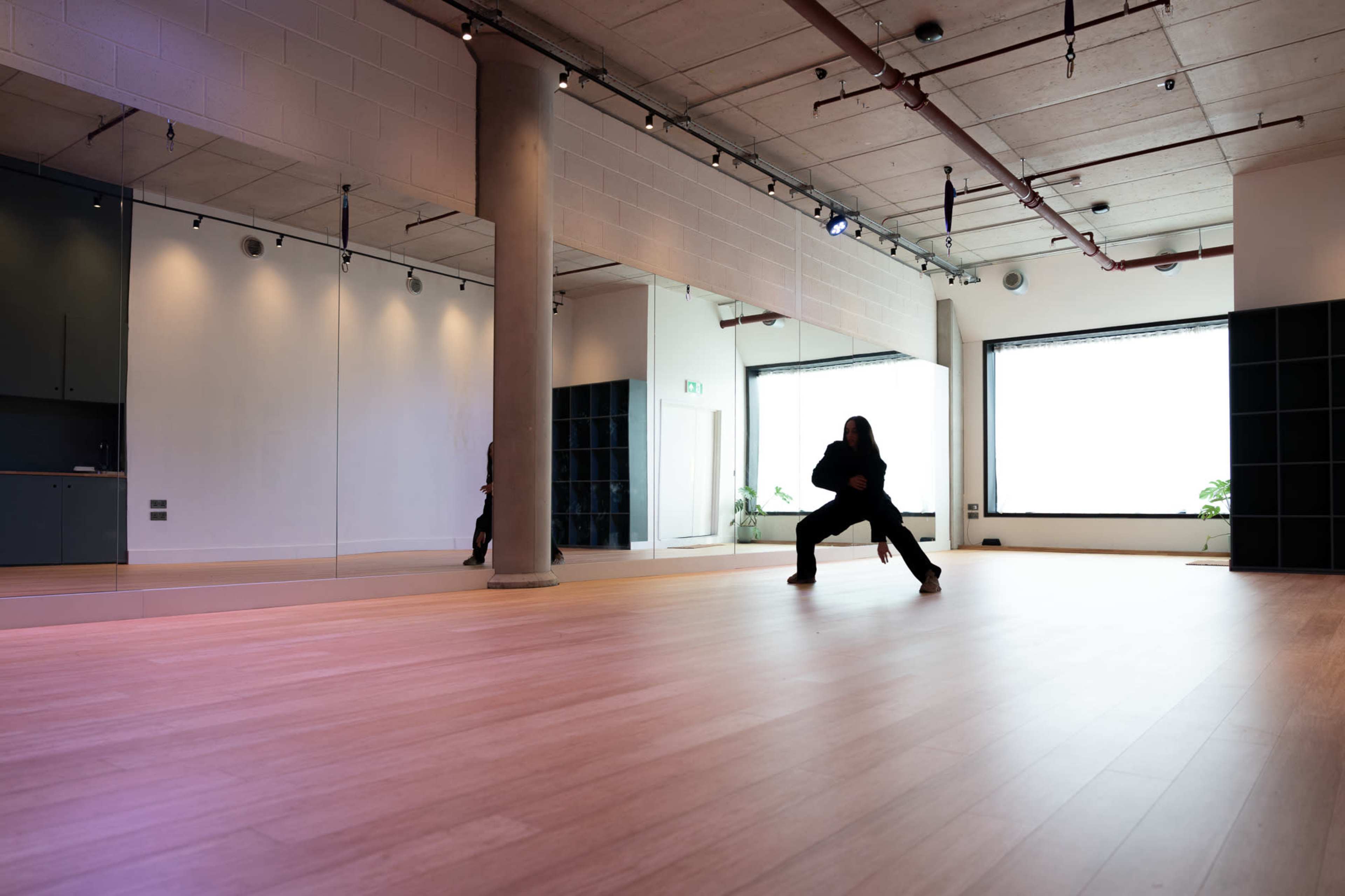 A person is practicing a martial arts stance in a spacious studio with large mirrors and wooden flooring.