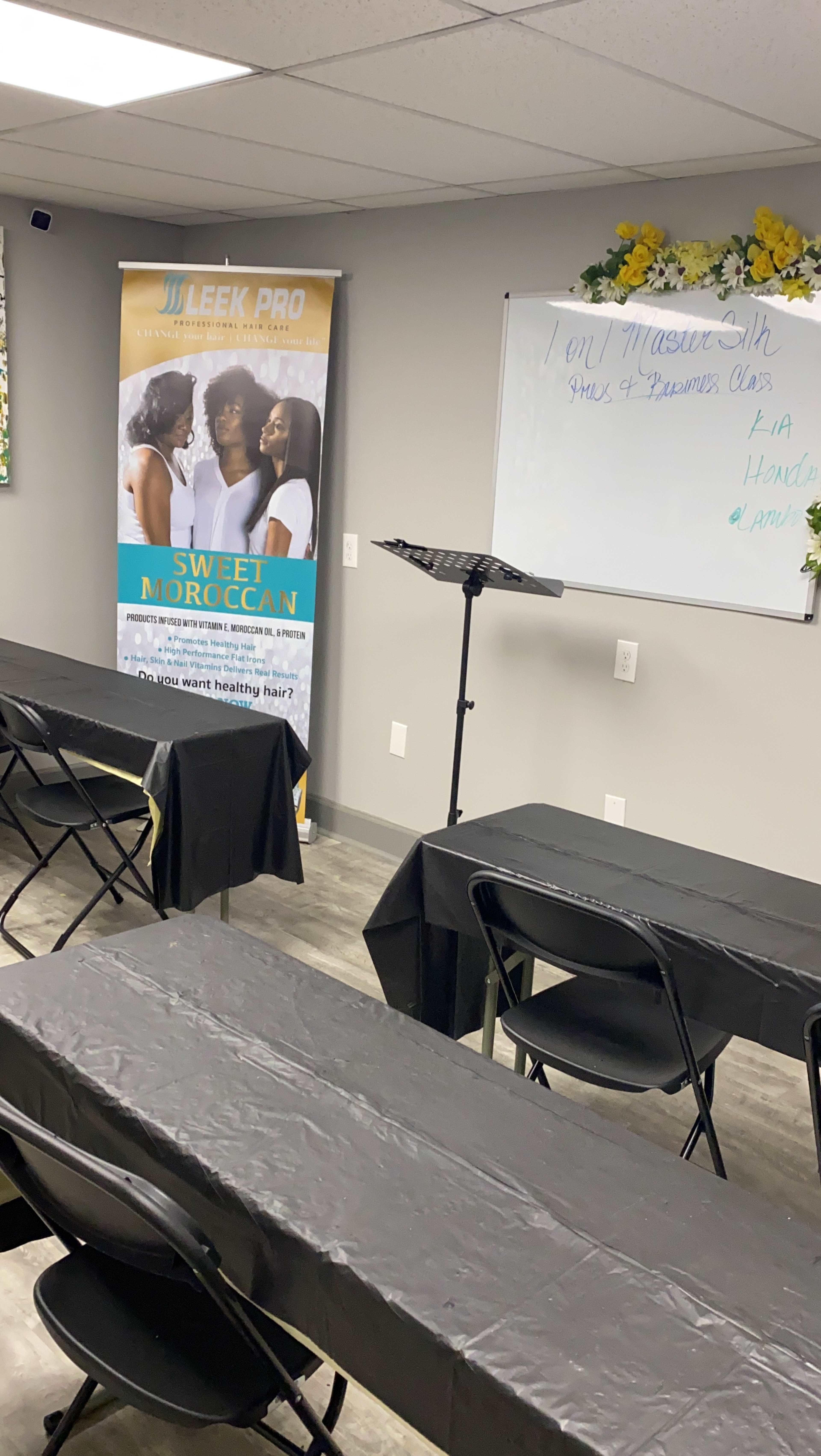 A classroom setup with rows of black tables and chairs, a banner for "Sweet Moroccan" on one side, and a whiteboard displaying a schedule of classes and names.