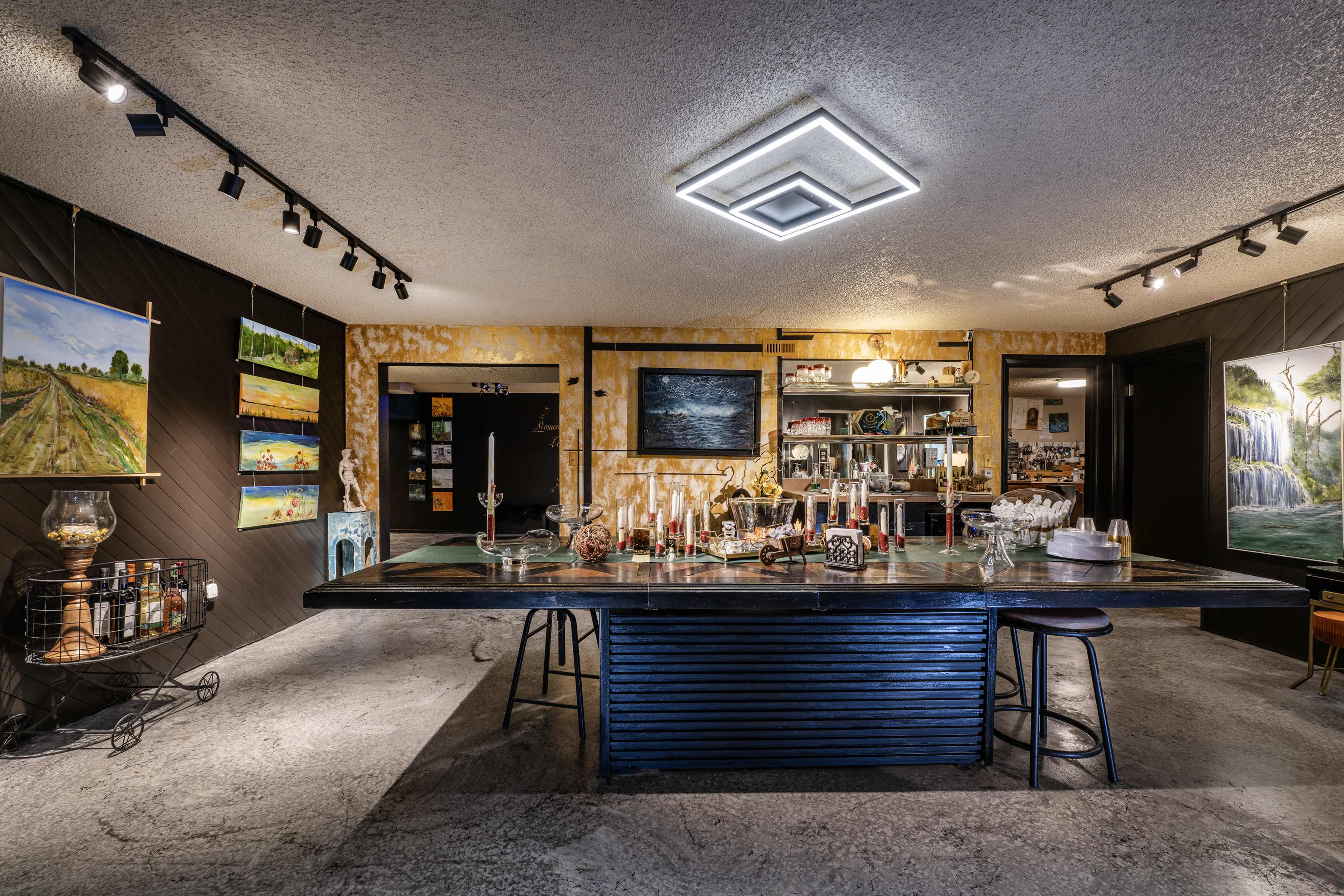 A well-lit bar area features a long counter with various bottles and glassware, surrounded by colorful artwork on the walls.