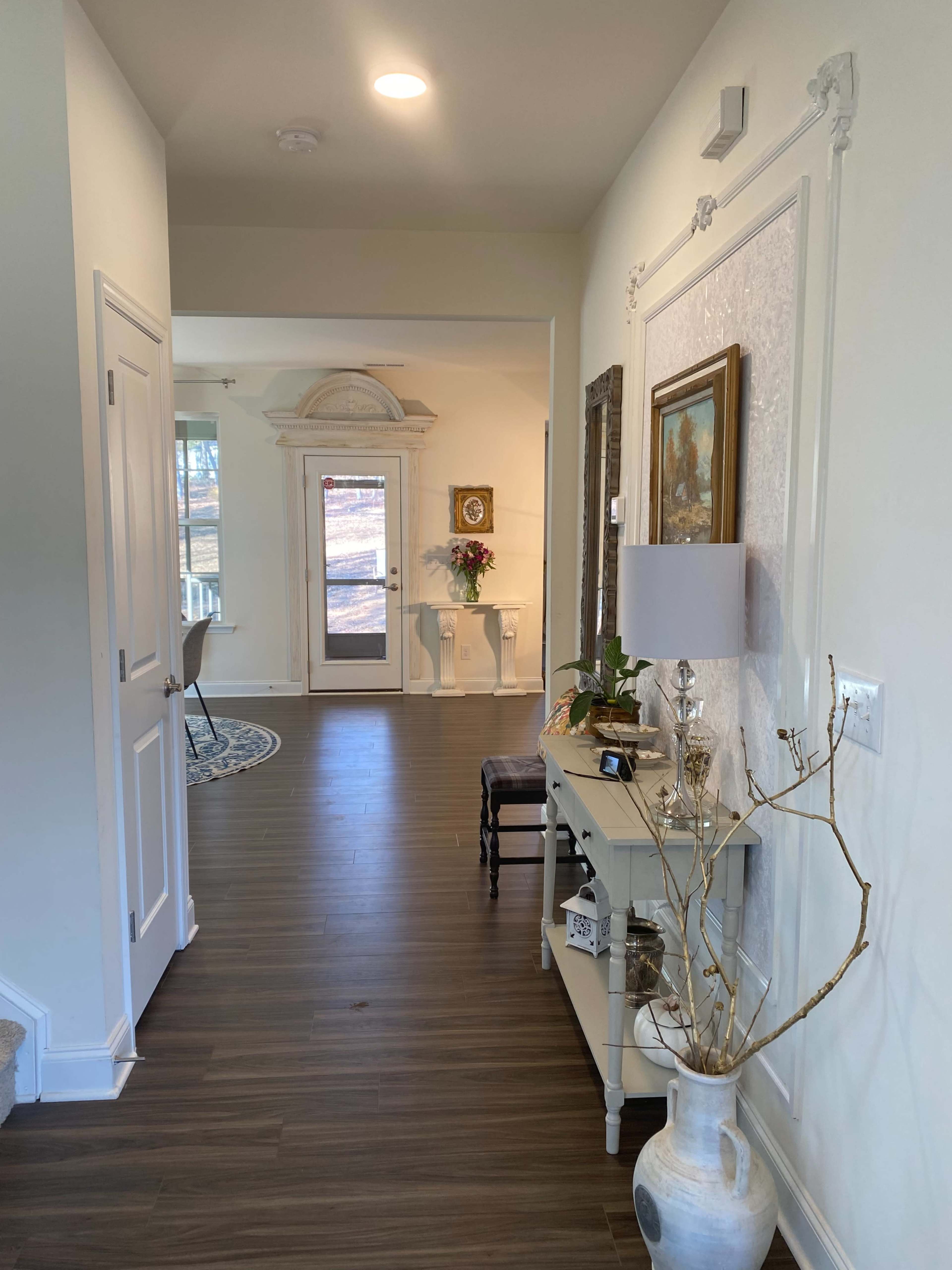 A hallway features a console table with decor, leading to a door with a window and a view of the outside.