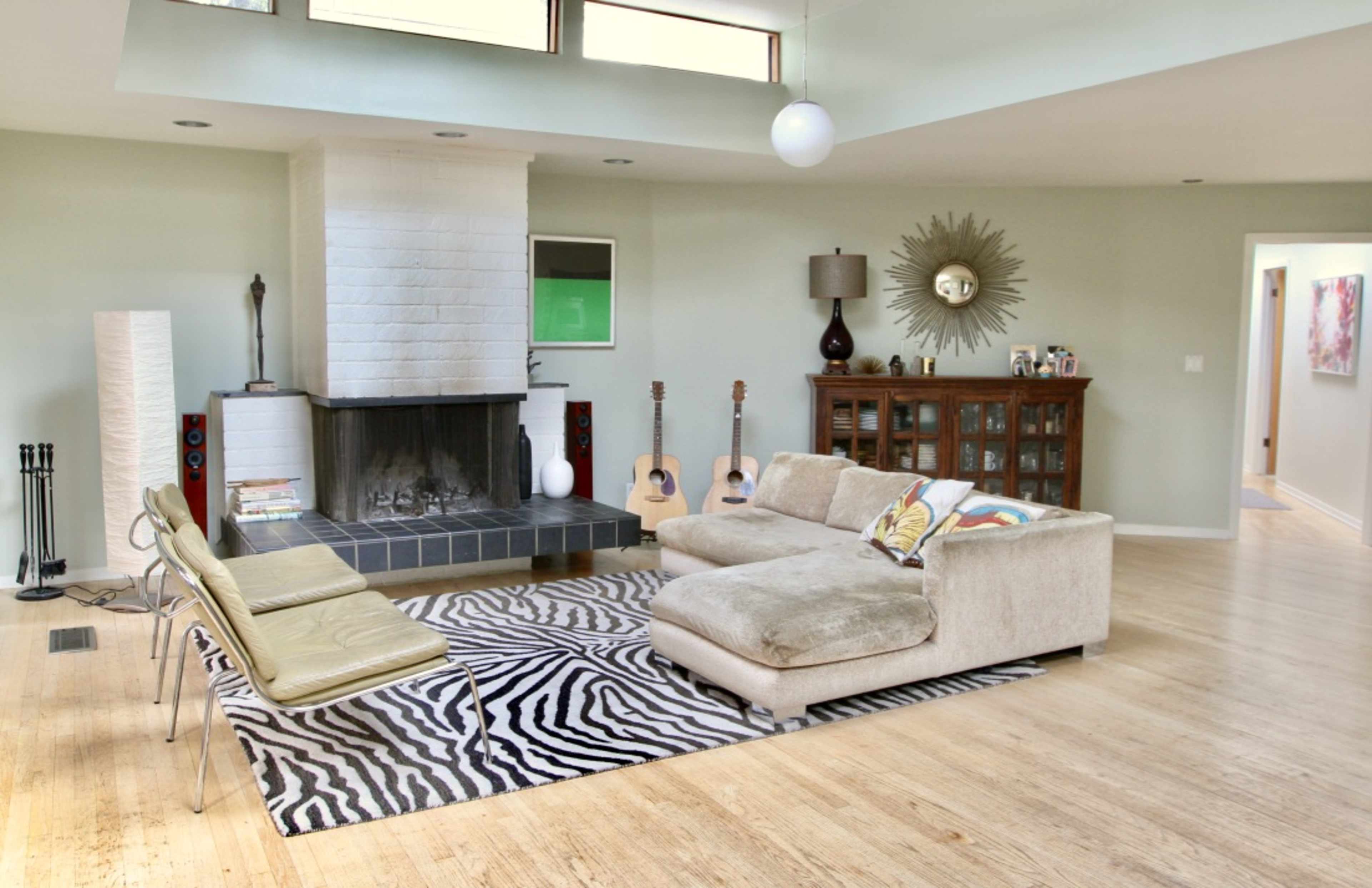 A spacious living room featuring a fireplace, a sectional sofa, a zebra-striped rug, and a combination of musical instruments and decorative furniture.