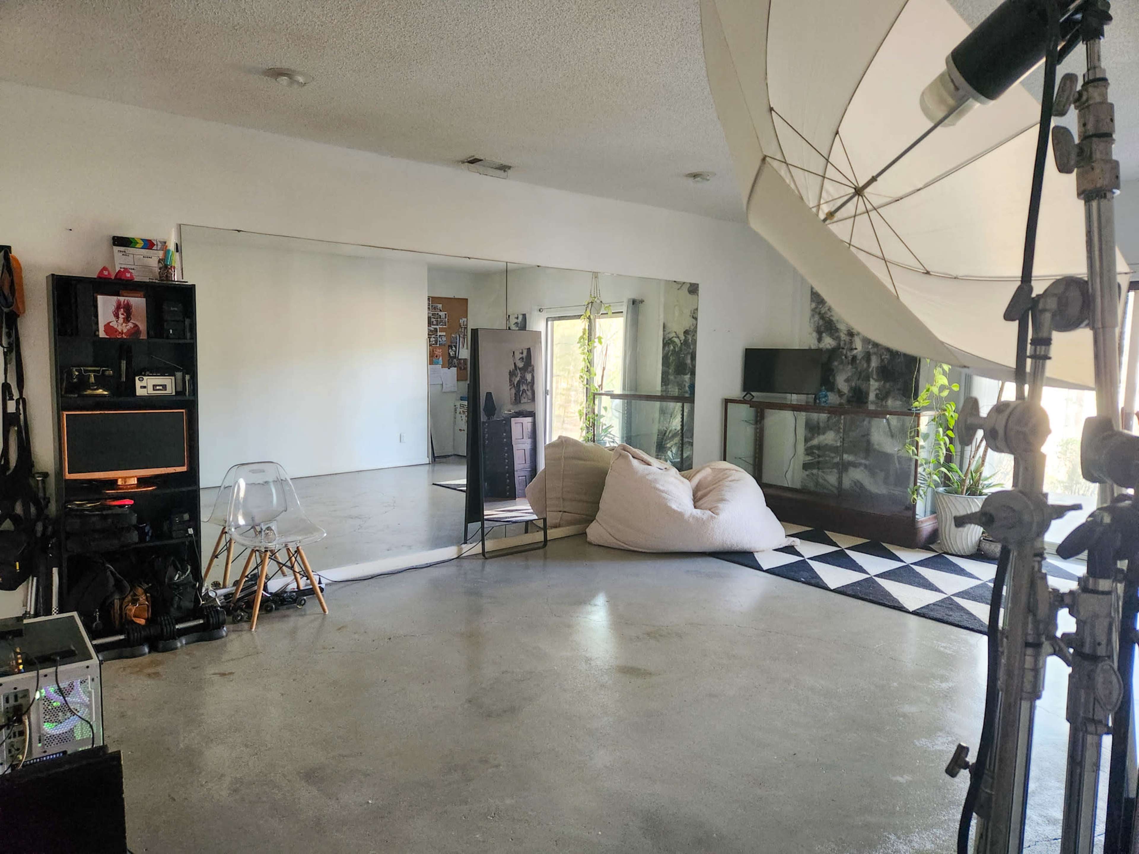 The room features a minimalistic design with a bean bag chair, a large mirror, a patterned rug, and various furniture and equipment against the walls.