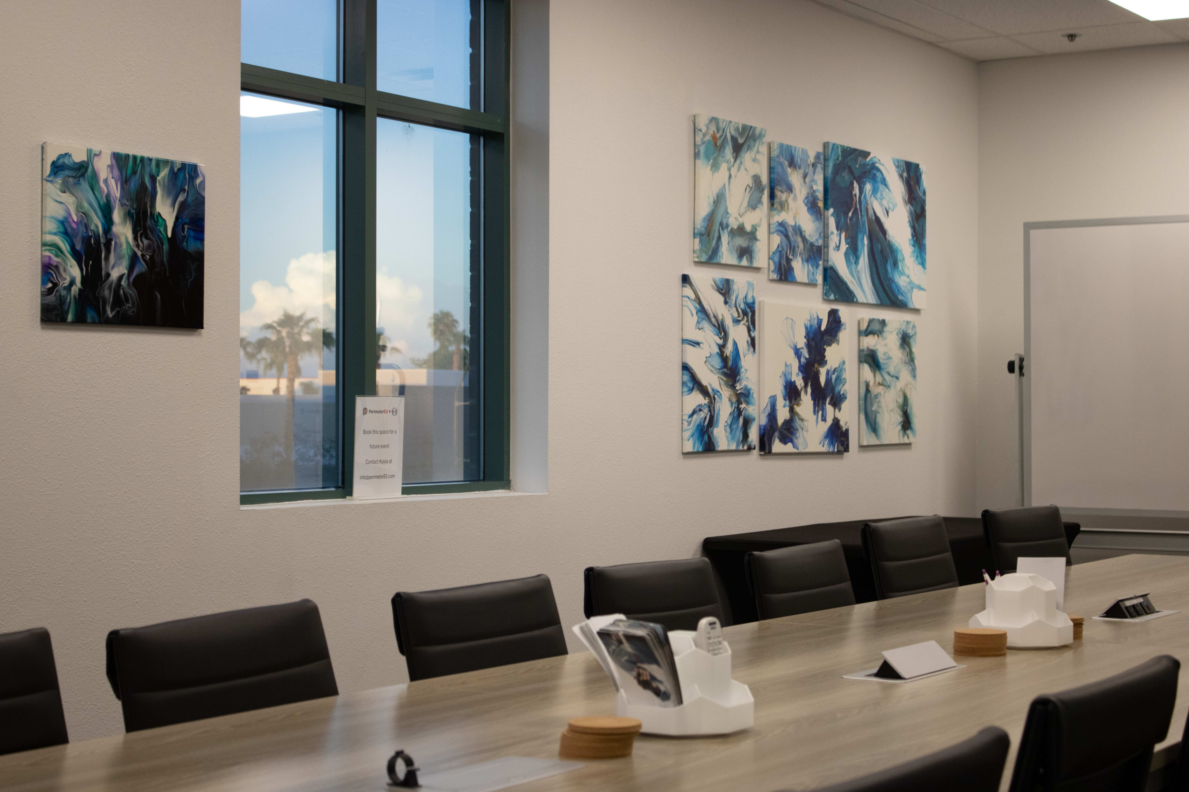 The image shows a modern conference room with a long wooden table, black chairs, and abstract artwork mounted on the walls.