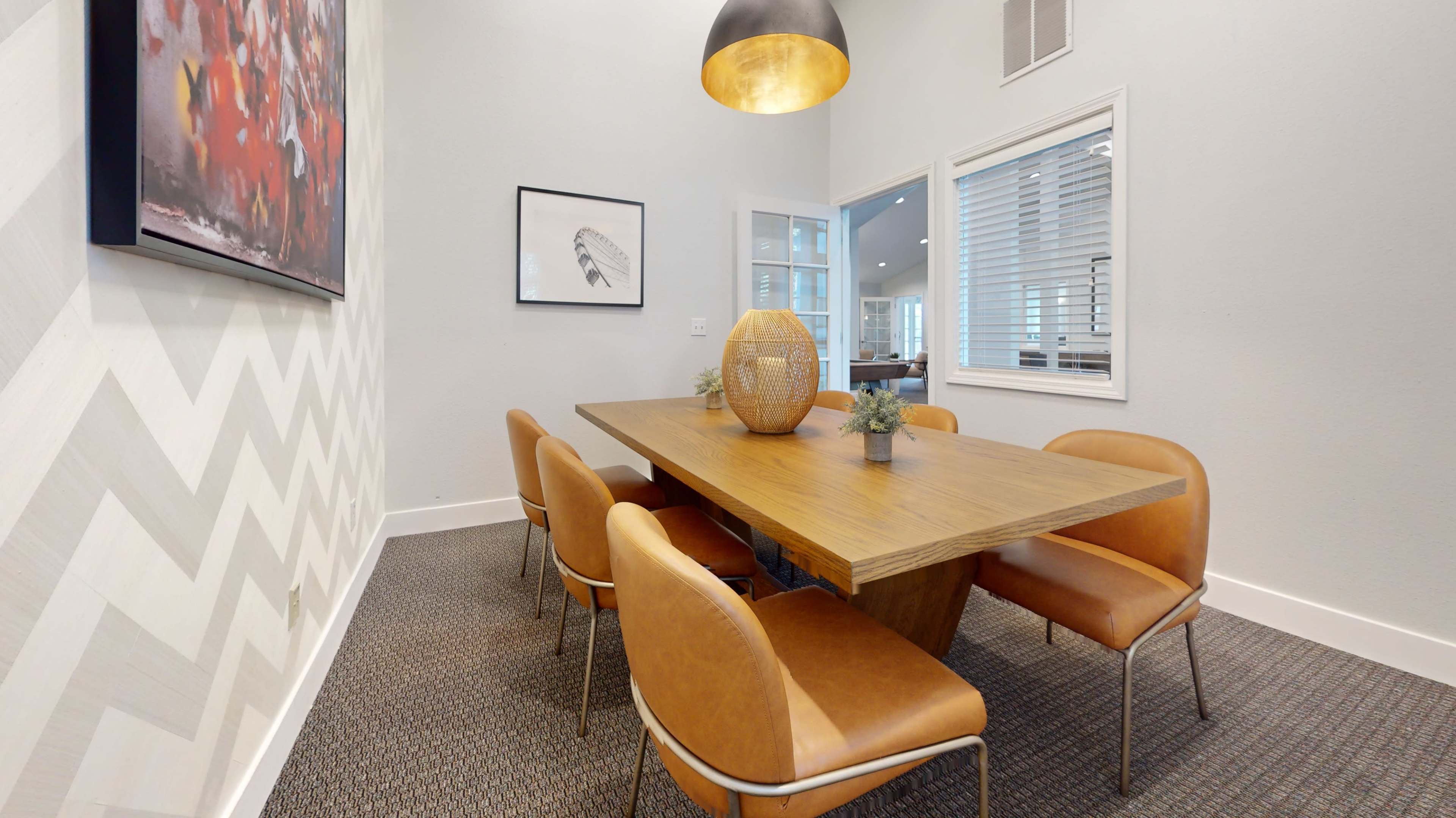 A modern dining area features a wooden table surrounded by brown leather chairs, with a pendant light hanging above and wall art on display.