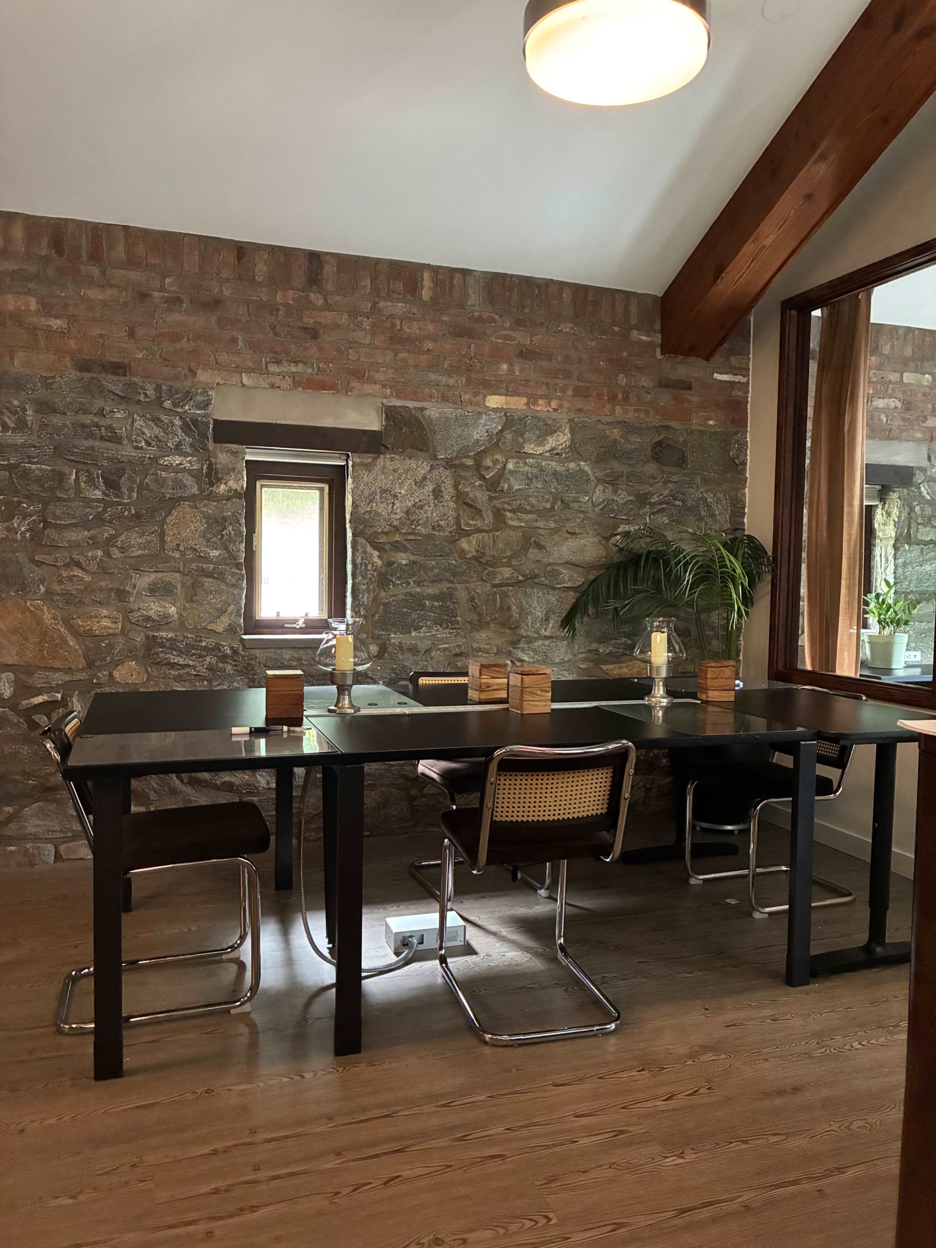 The image shows a modern dining area featuring a black table surrounded by sleek chairs, with a stone and brick wall in the background.