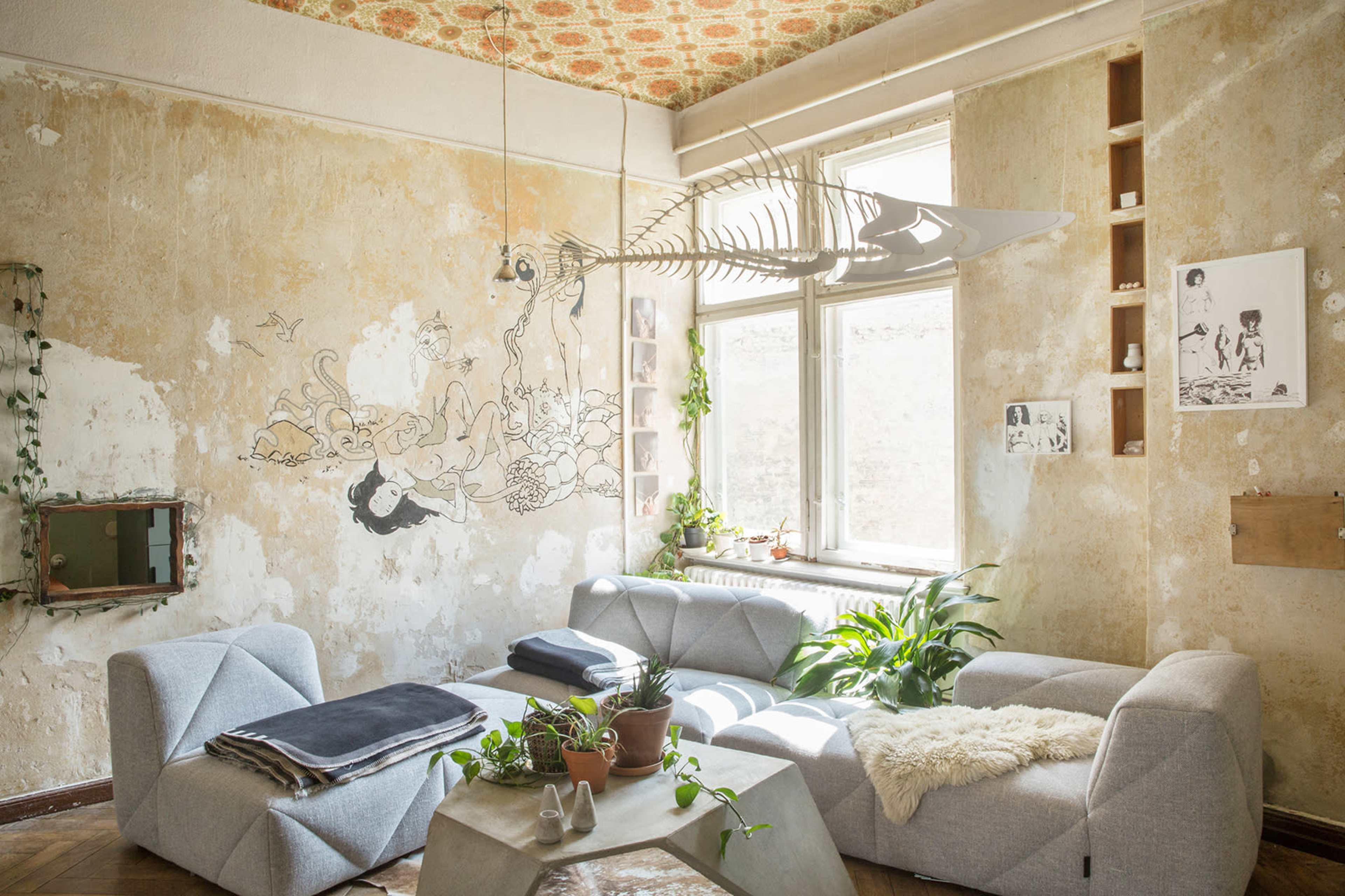 The image shows a living room featuring two modern gray sofas, a large window with natural light, and decor elements like plants and wall art.