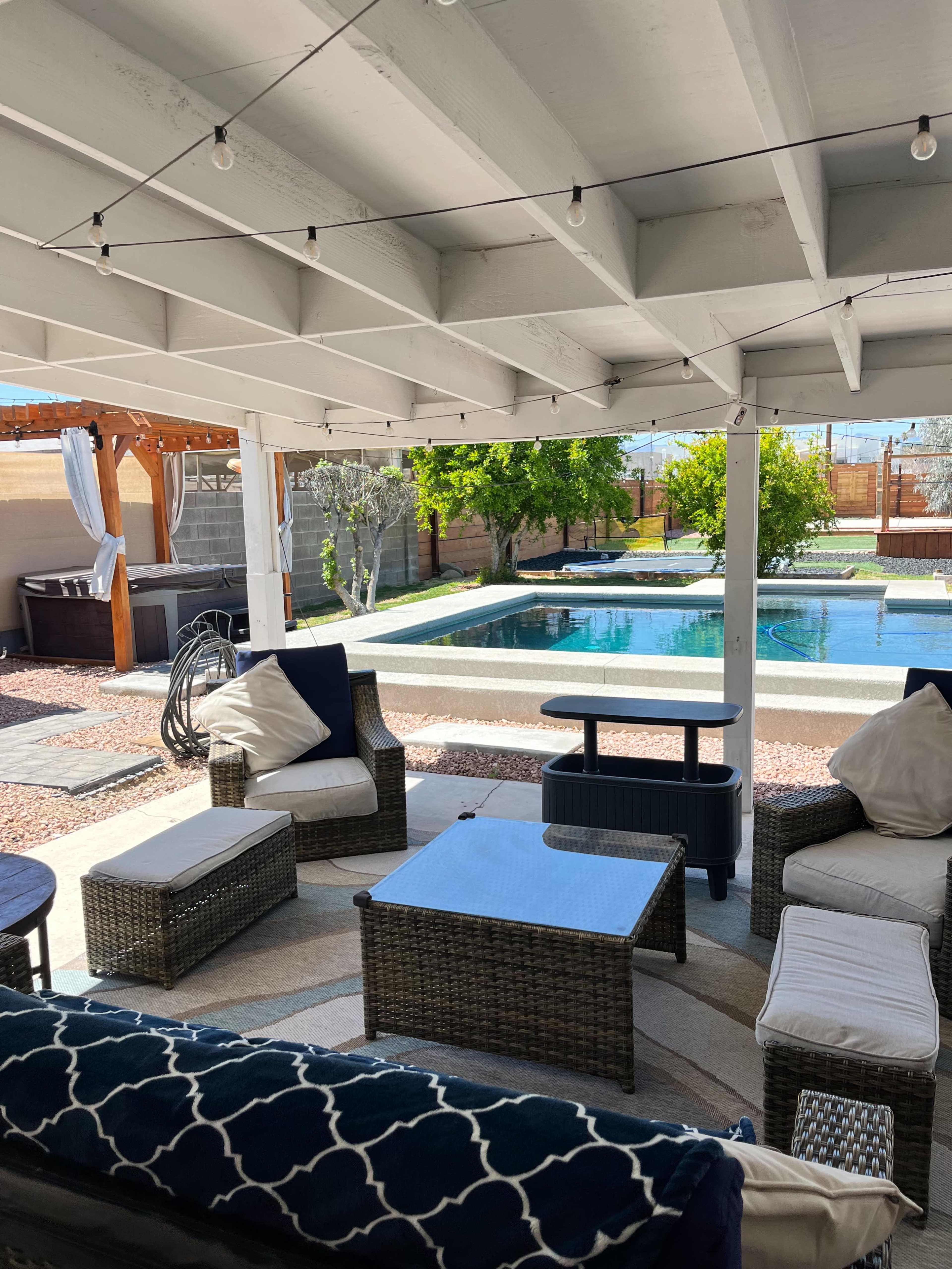 A covered outdoor seating area with woven furniture surrounds a small table, overlooking a pool and landscaped backyard.