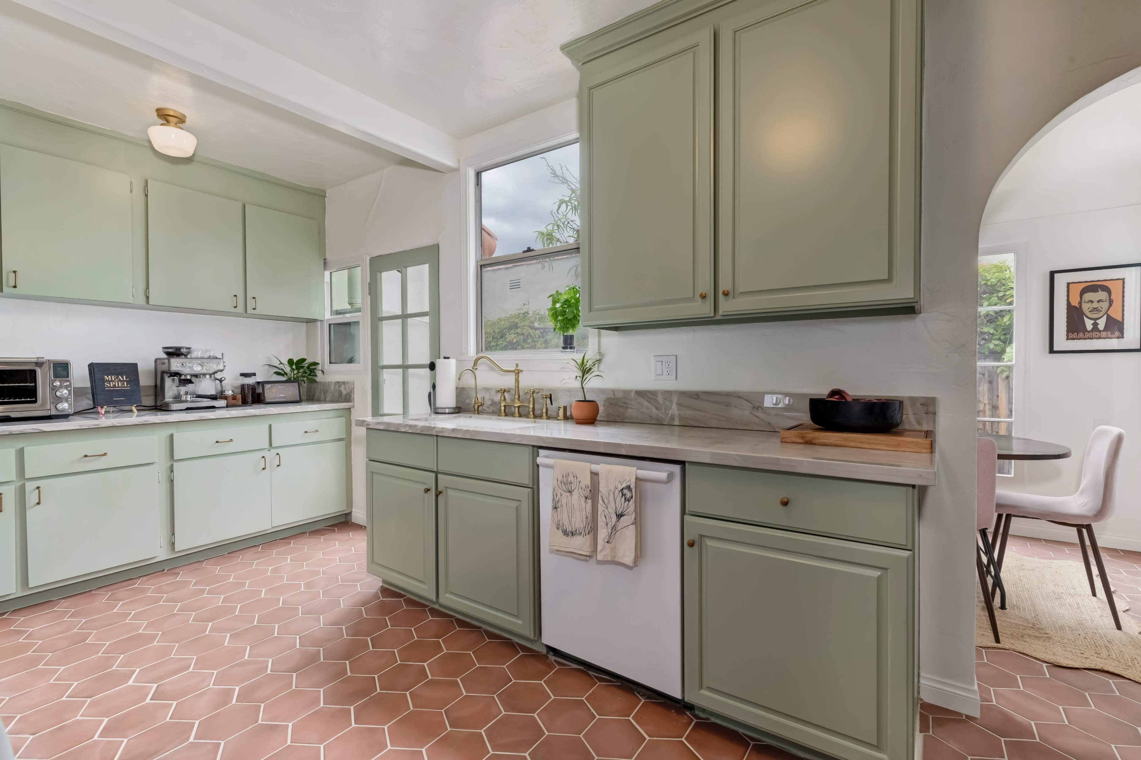 The kitchen features light green cabinets, a beige countertop, and a hexagonal tile floor with a visible dining area nearby.