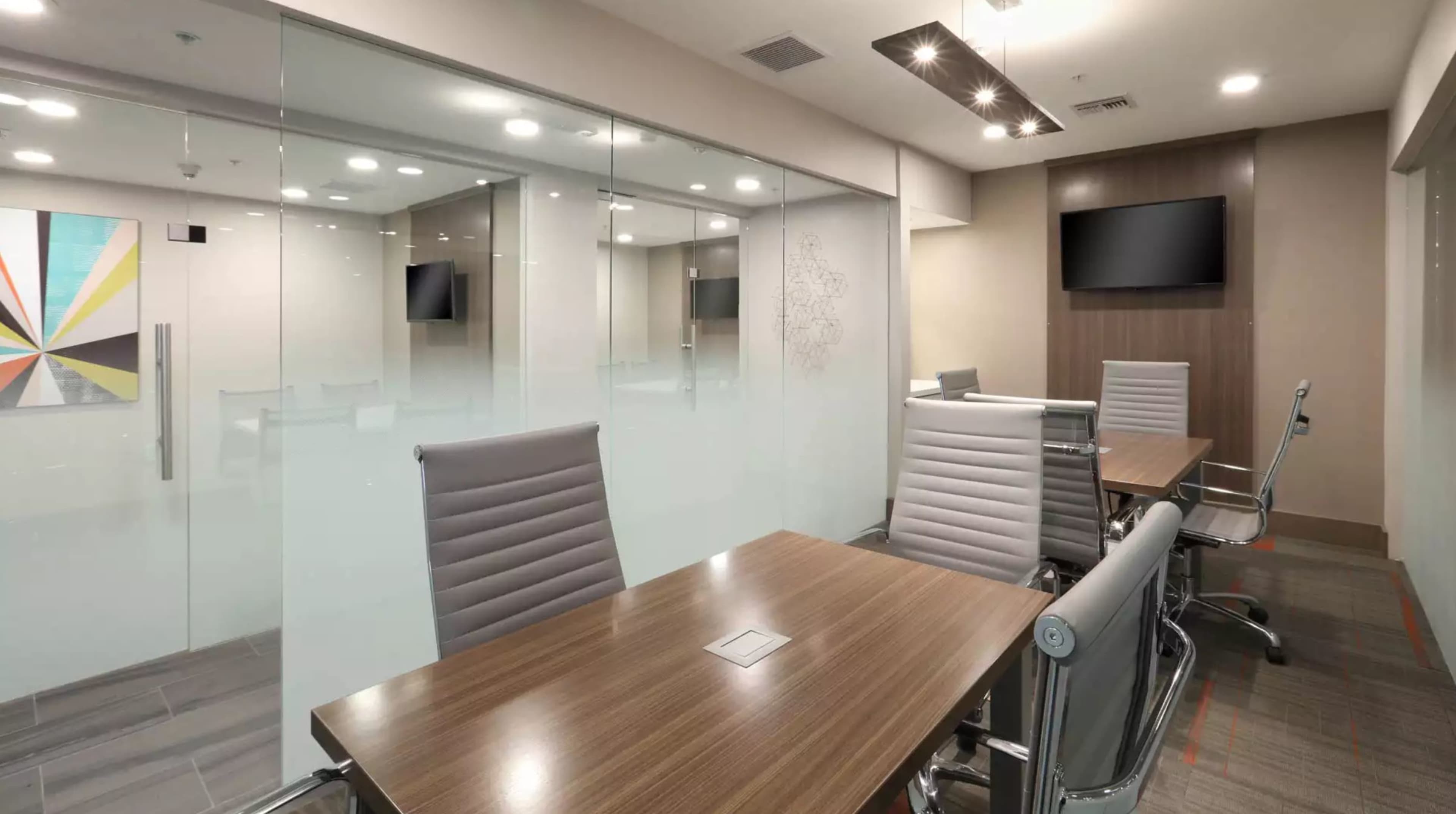 A modern conference room with a wooden table, ergonomic chairs, and glass walls.