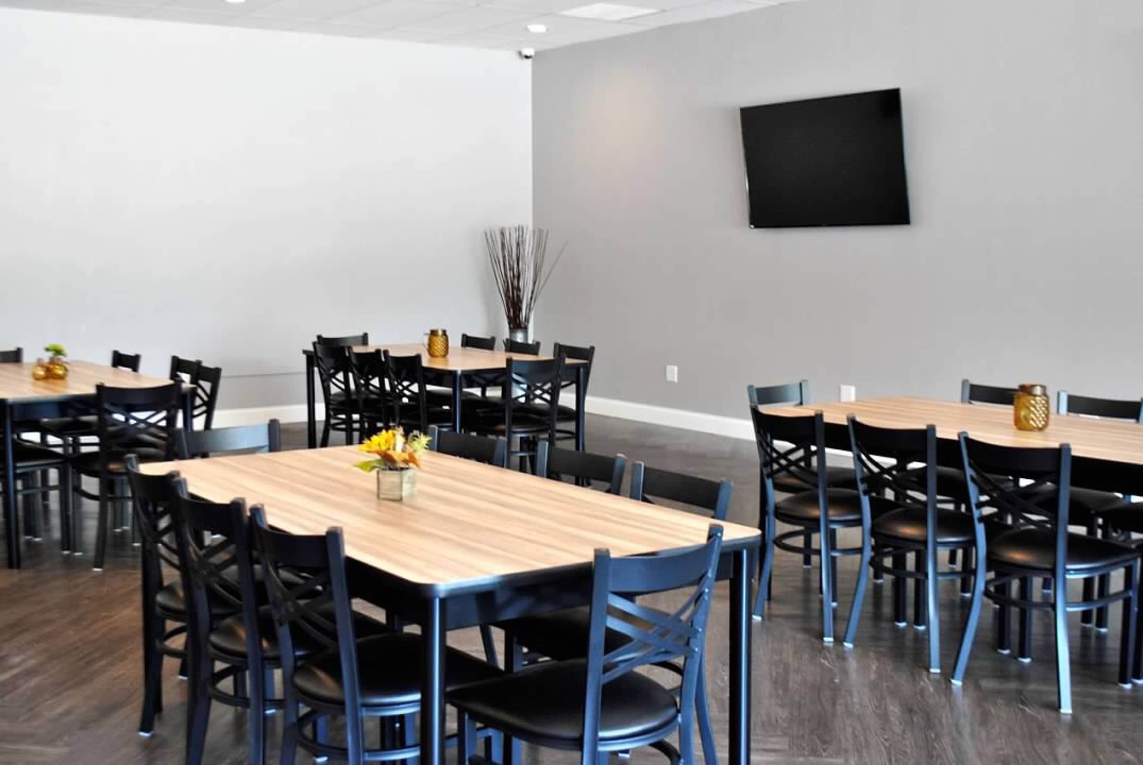 A spacious dining area with several tables set up in a light-colored room, featuring a television mounted on the wall.