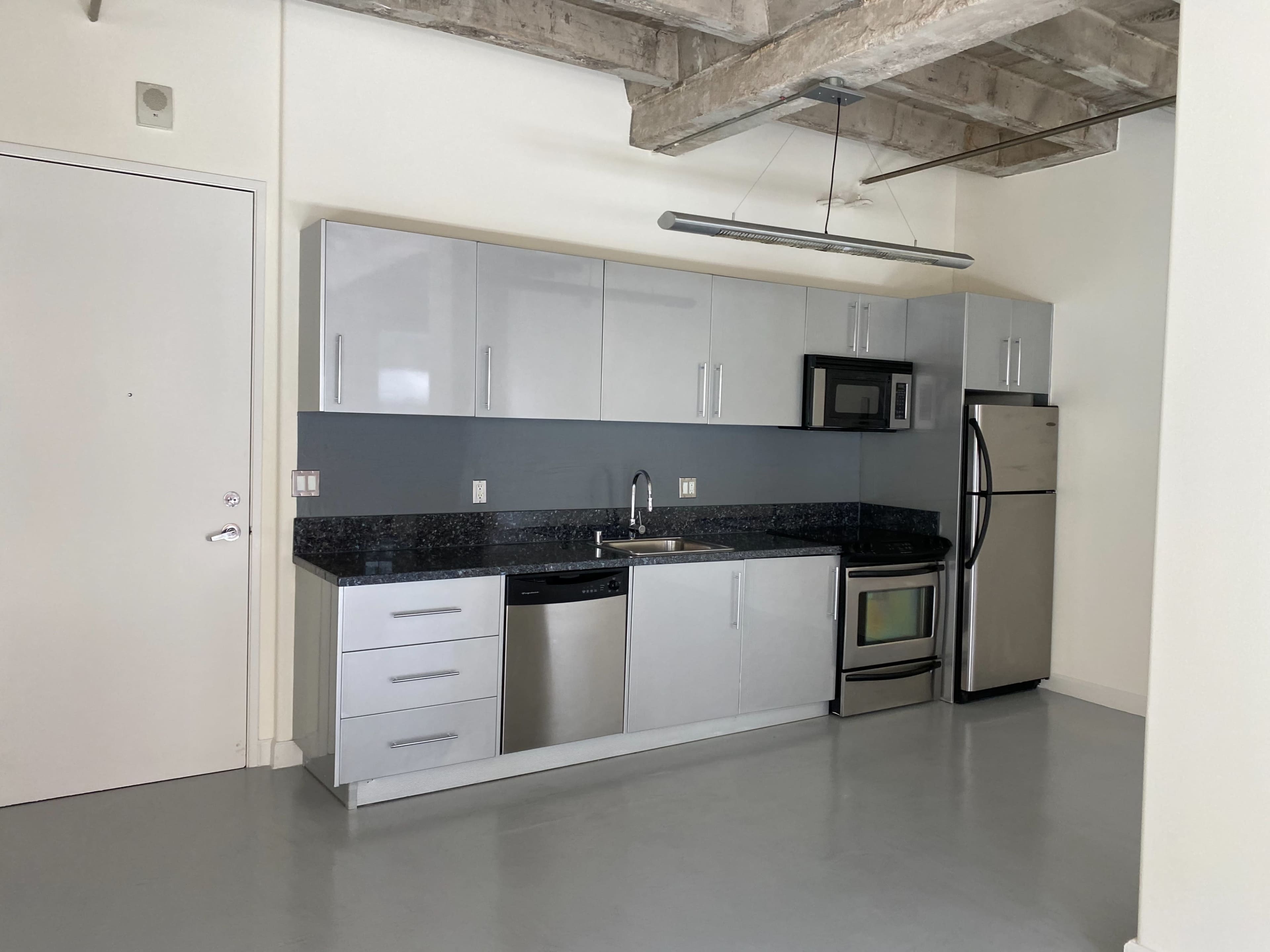 The image depicts a modern kitchen with stainless steel appliances, gray cabinets, and a black countertop.