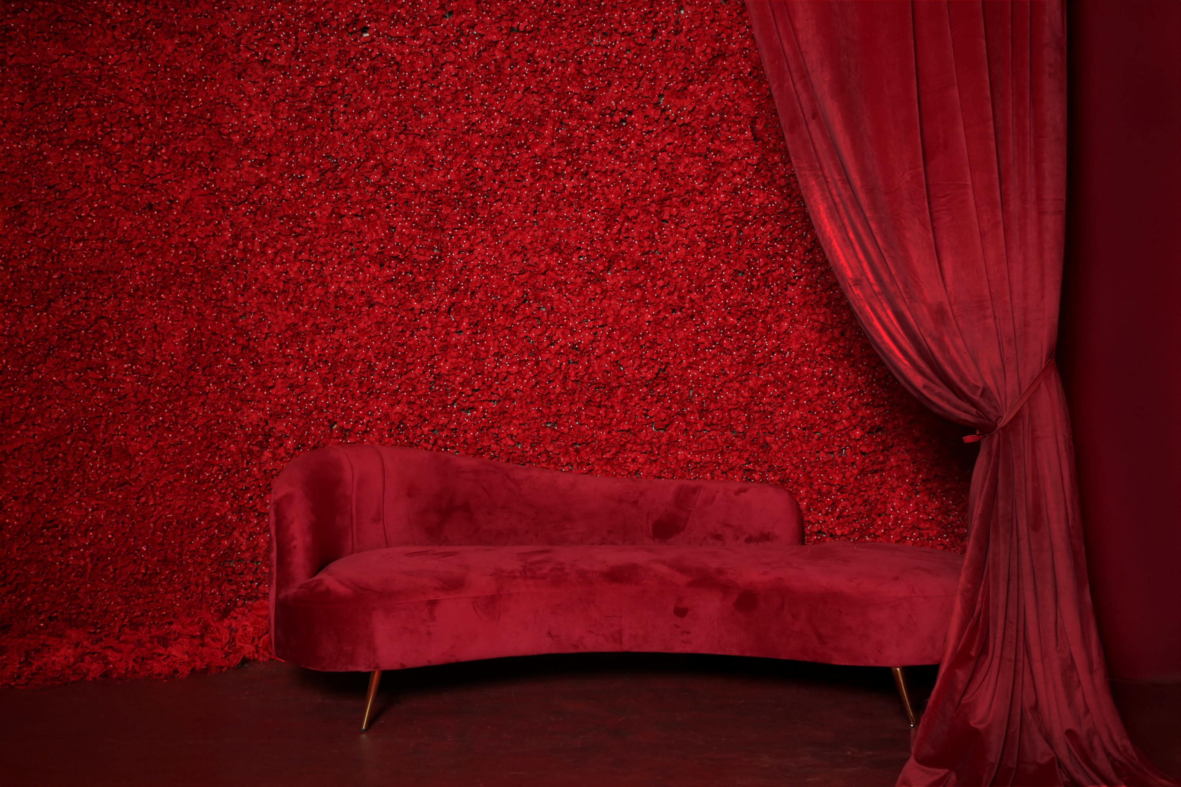 The image shows a red velvet couch in front of a textured red wall, complemented by a flowing red curtain.