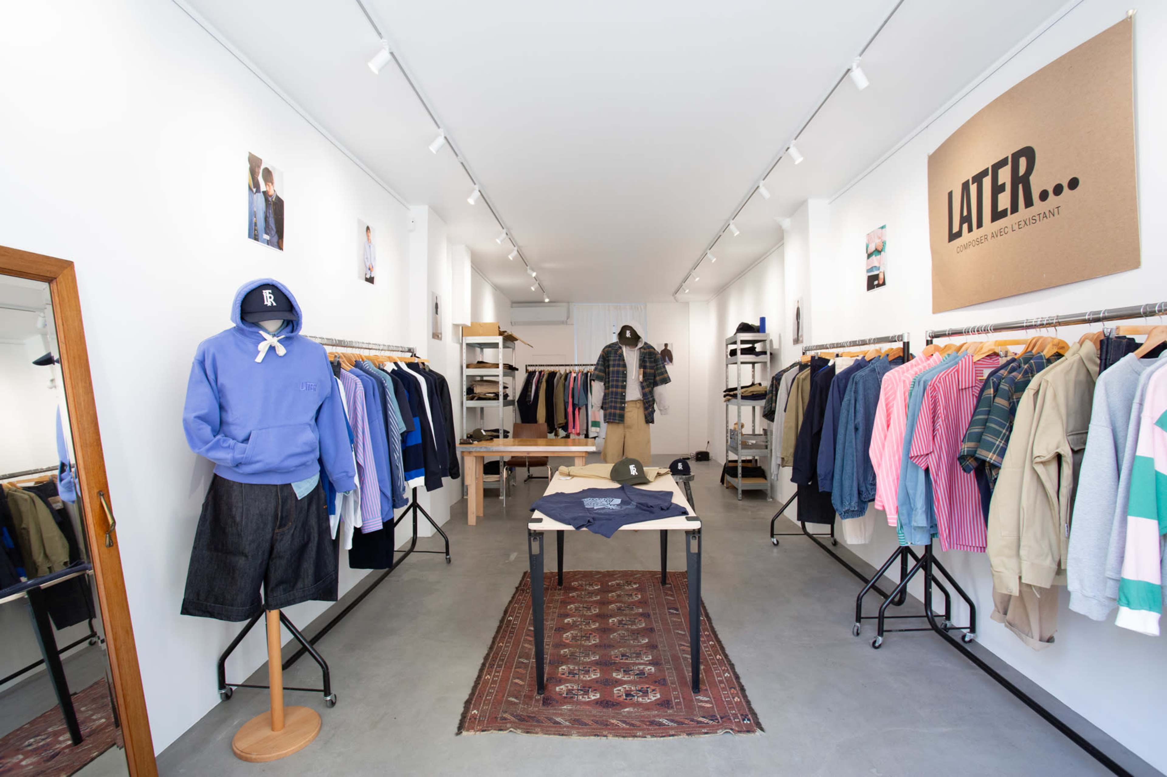 The image shows a clothing store interior with racks of various garments on display and a central table featuring folded apparel.