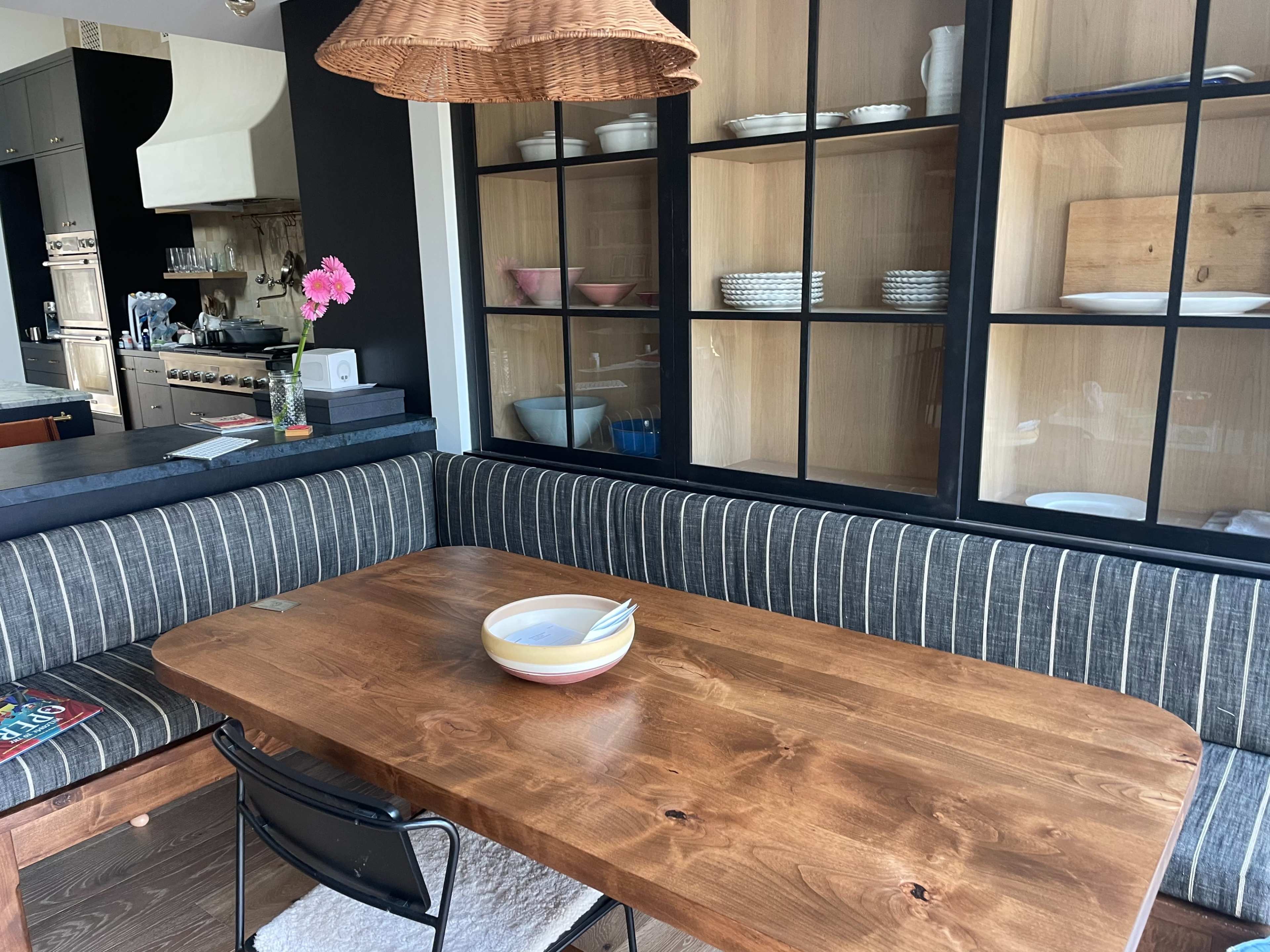 The image shows a dining area with a wooden table, striped bench seating, and a glass-fronted cabinet displaying dishware.