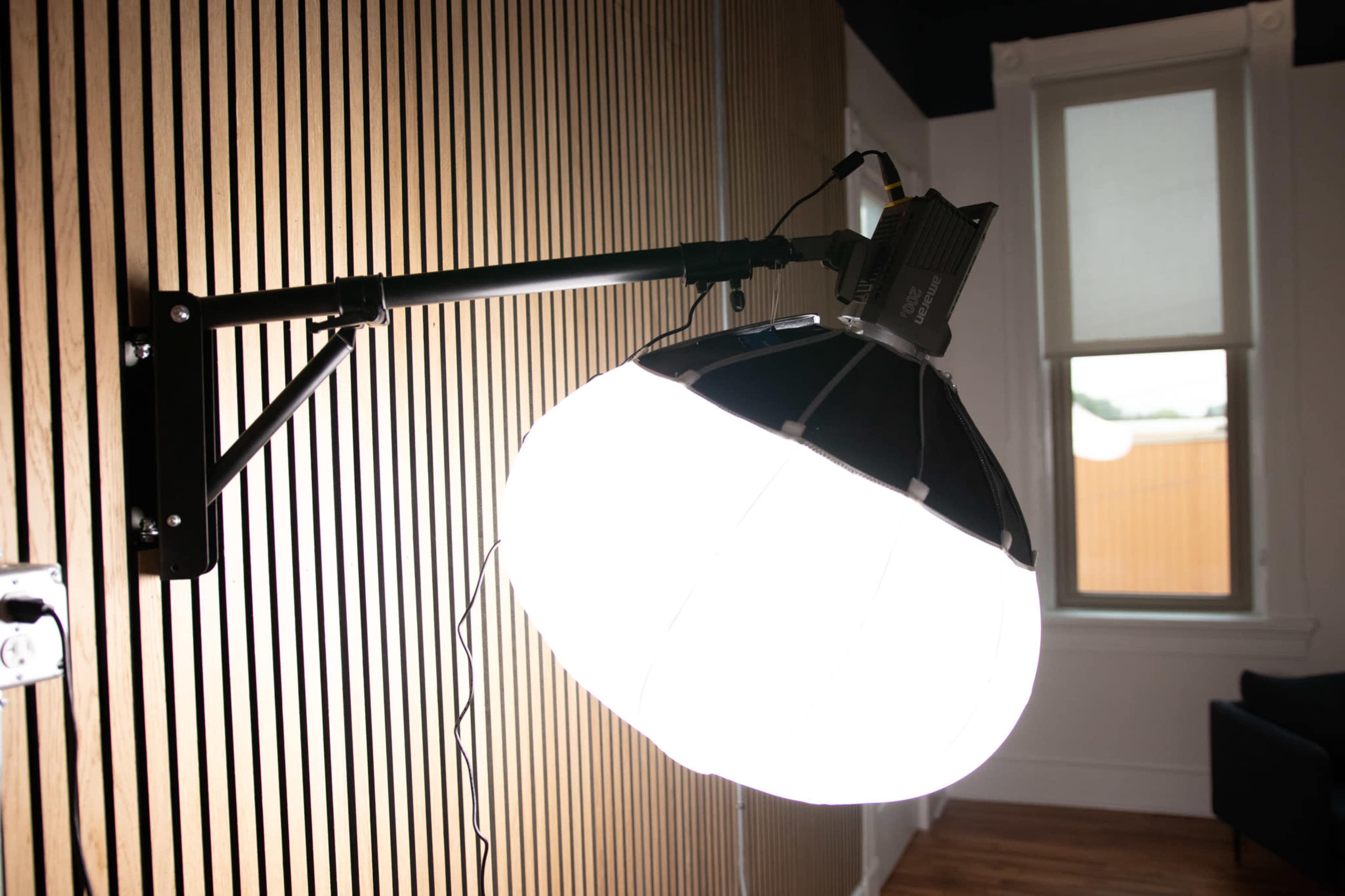 A large, round light fixture is mounted on a black arm, positioned against a wooden slatted wall.
