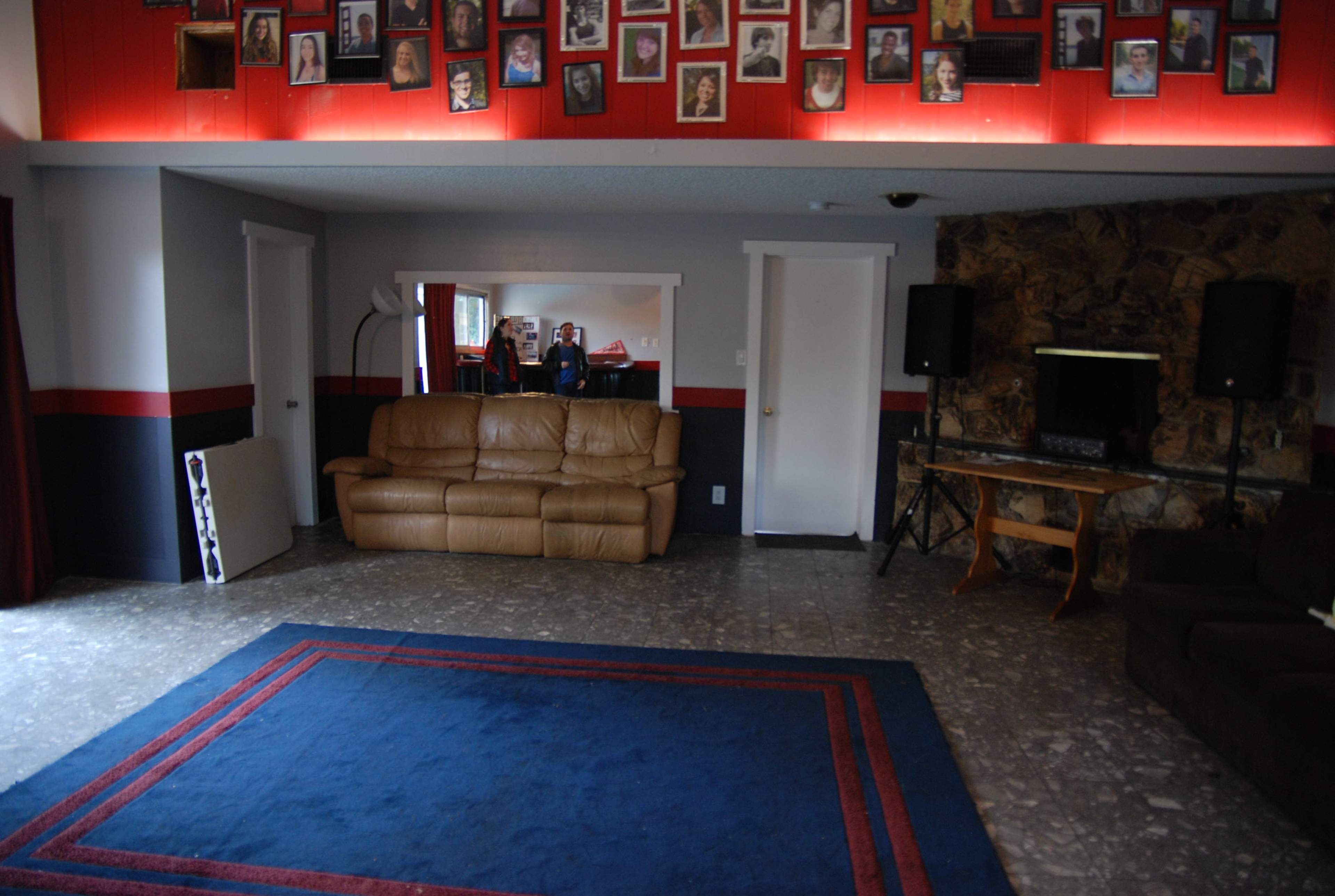 A spacious room with a blue rug, brown leather couch, a green couch, and a wall adorned with a grid of framed photographs.