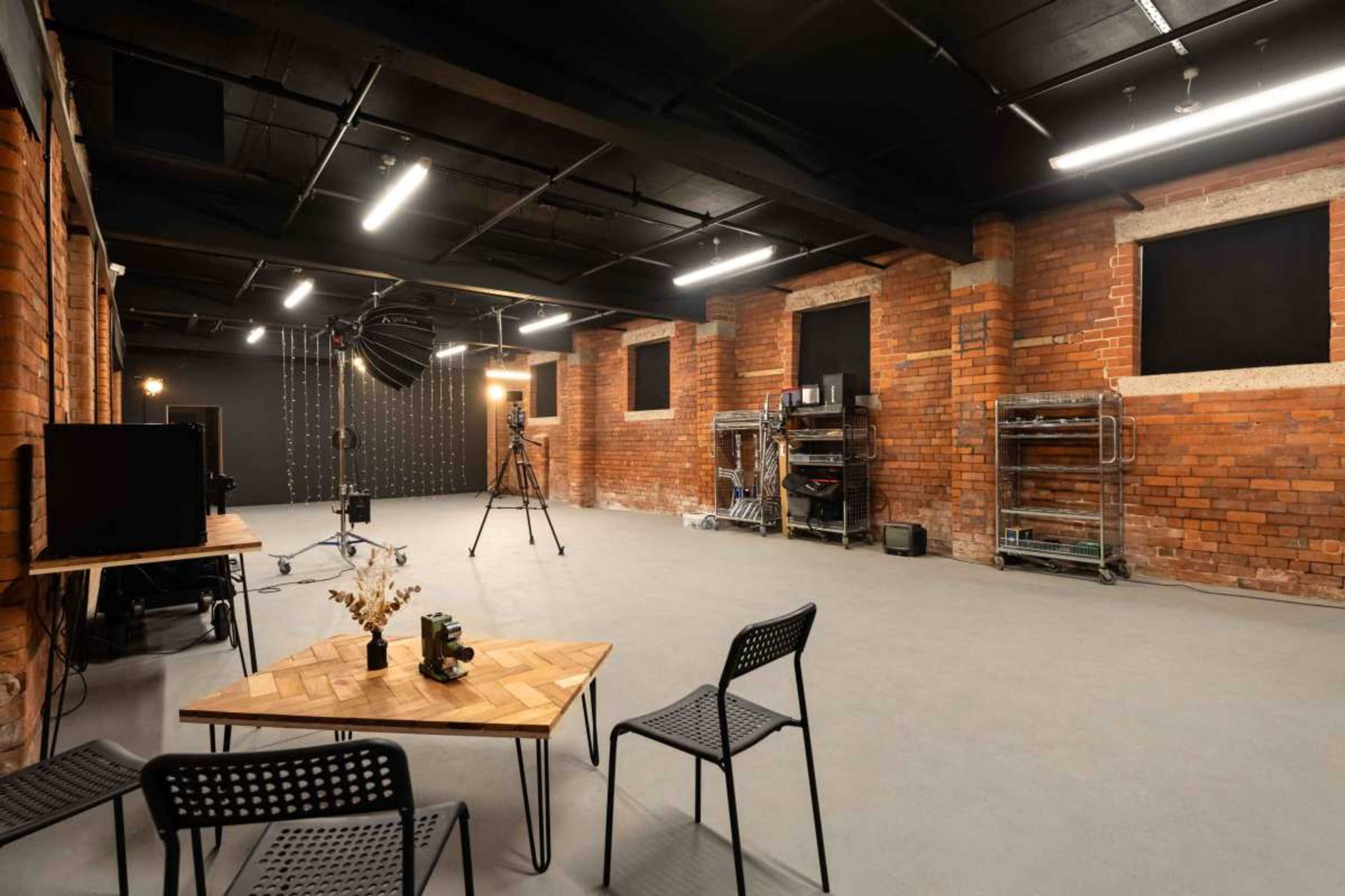 The image shows a spacious photography studio with exposed brick walls, a smooth gray floor, and various equipment set up, including light stands and a backdrop.