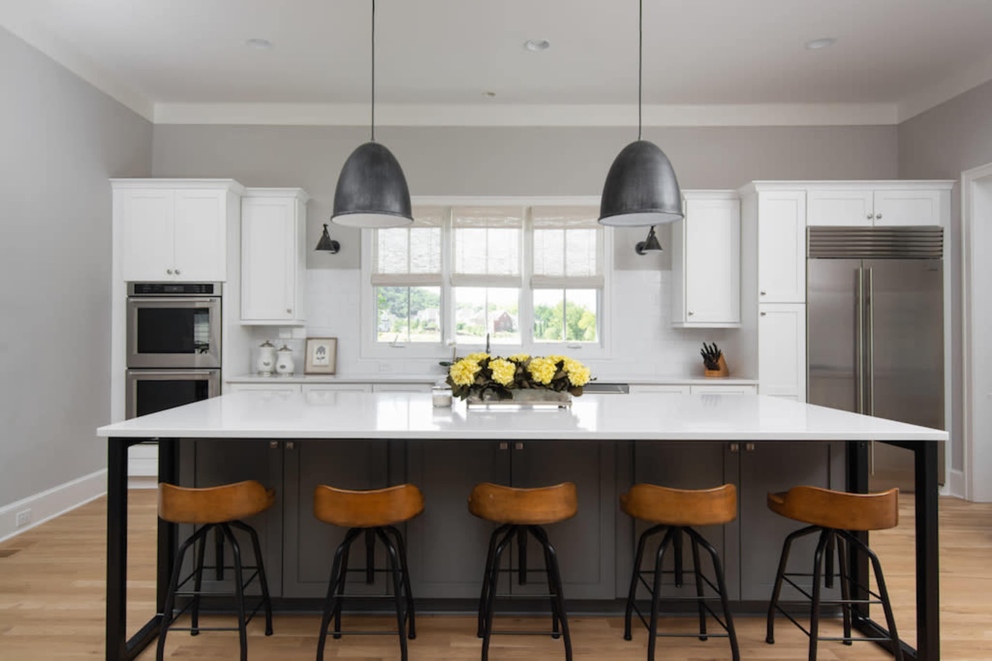 A modern kitchen features a large island with bar stools, white cabinetry, and pendant lighting above.
