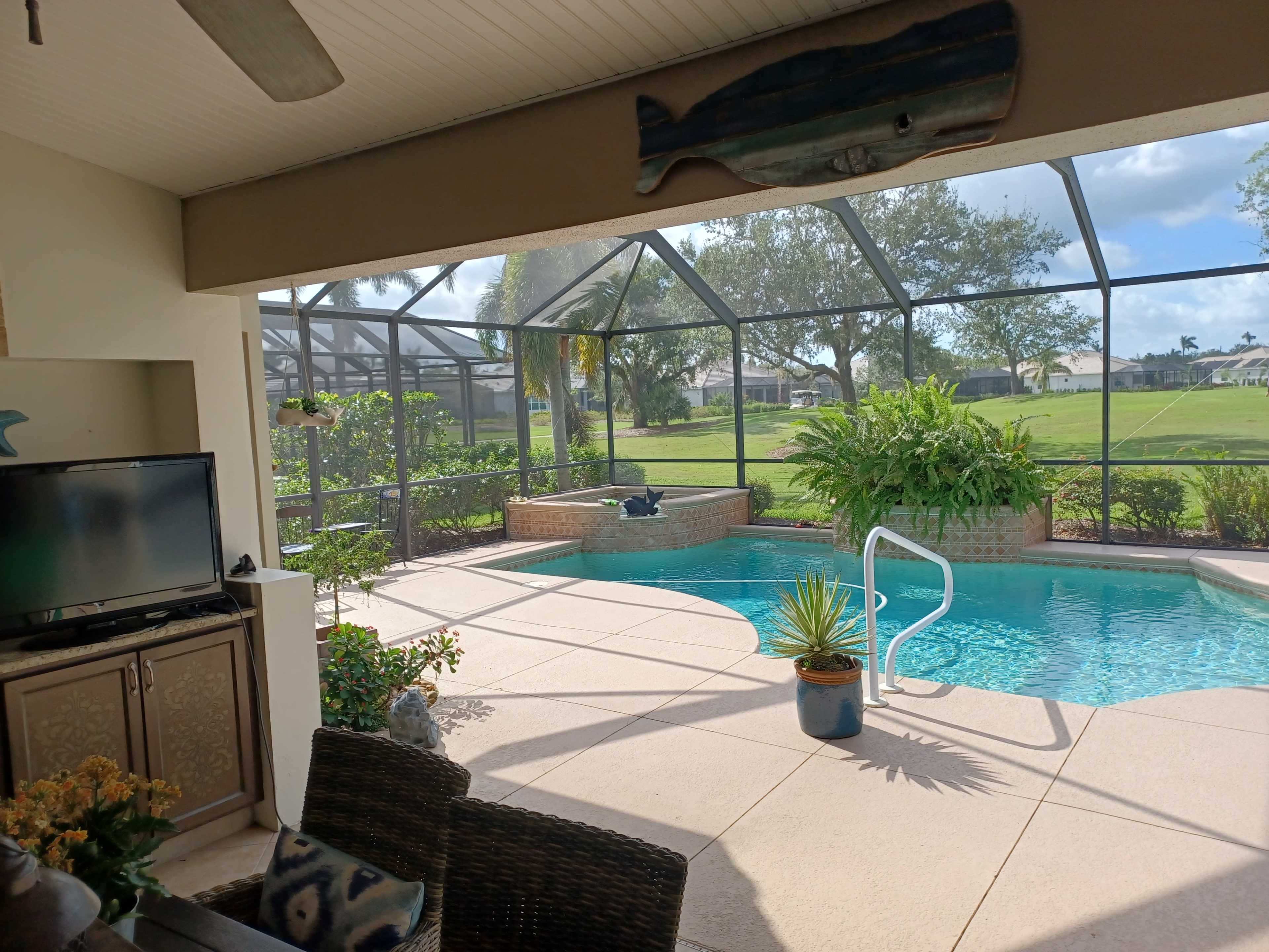 A covered patio overlooks a swimming pool surrounded by lush greenery and a screened enclosure.