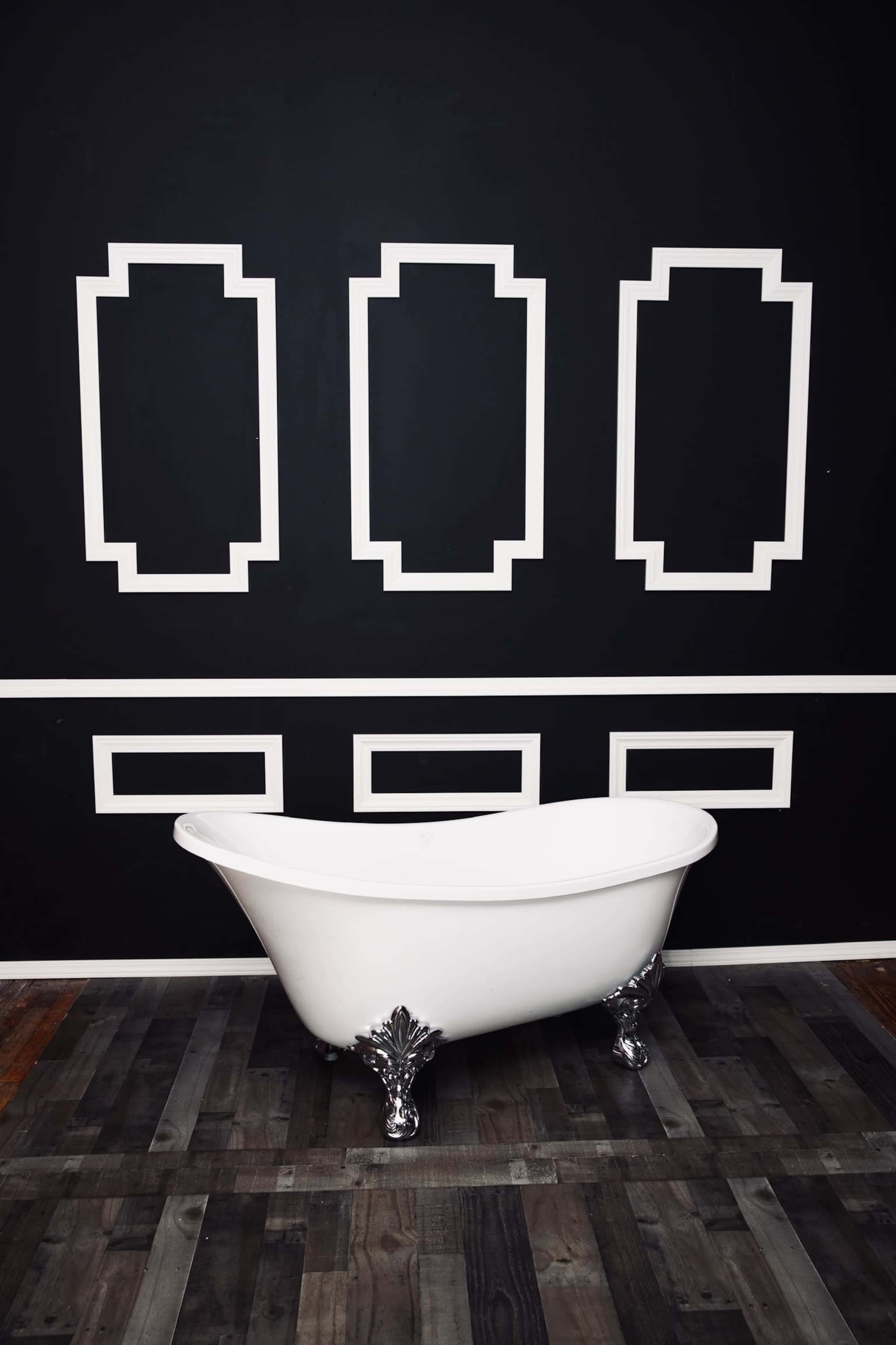 A white freestanding bathtub is positioned on a wooden floor against a black wall featuring white geometric paneling.