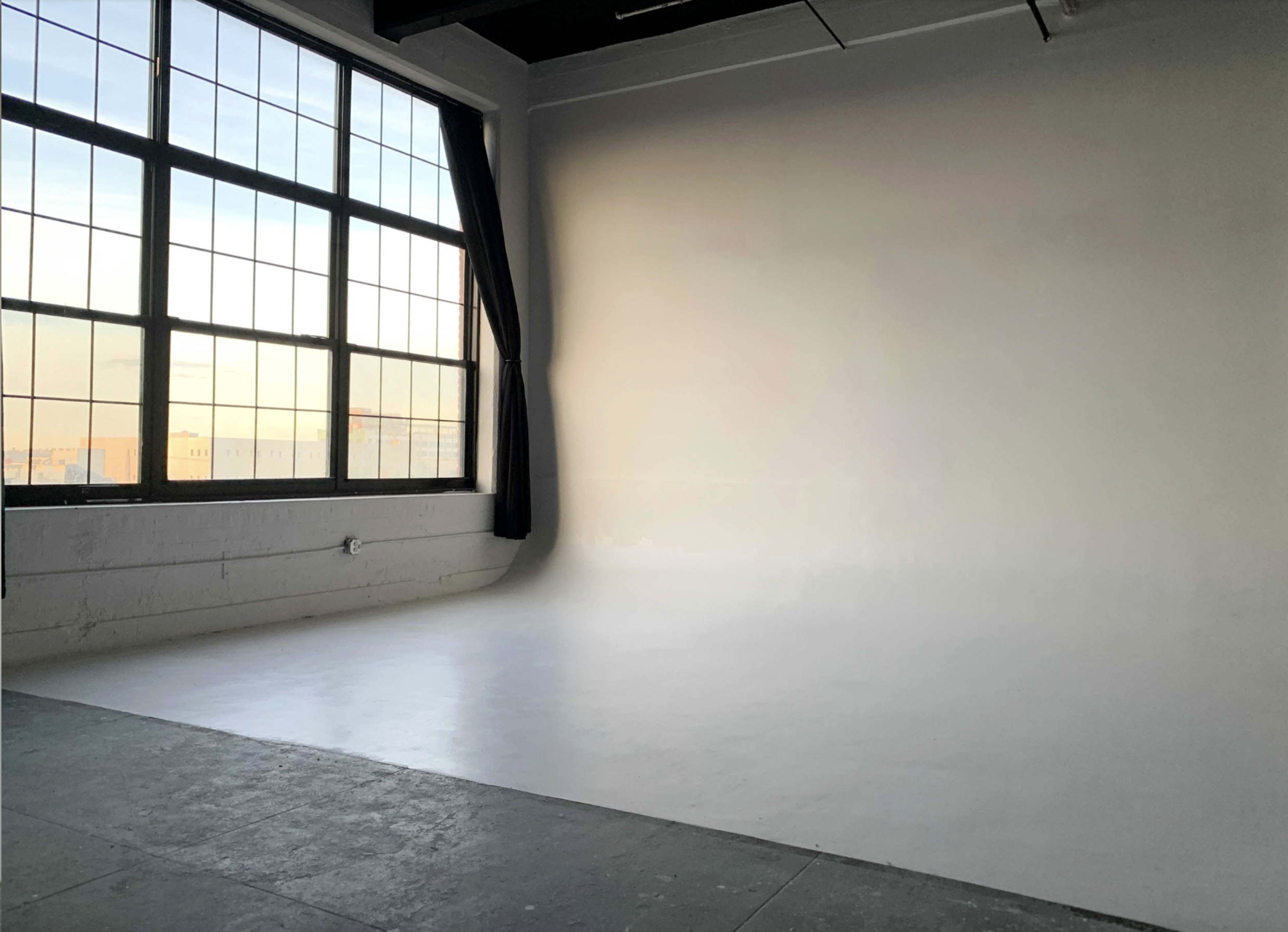 The image shows a spacious, empty photography studio with large windows allowing natural light to enter.