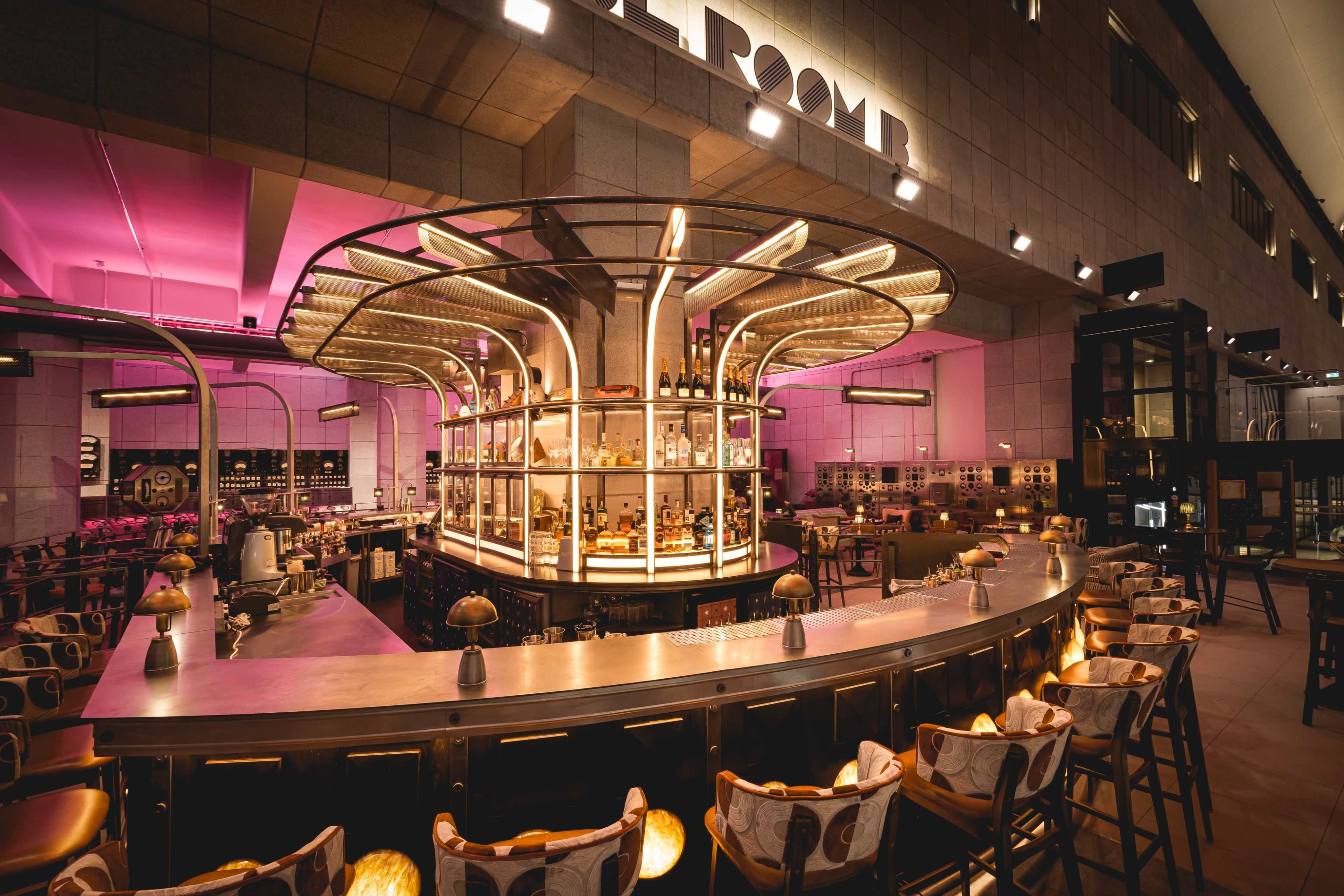 A modern bar area with a circular central bar surrounded by high stools, illuminated by soft lighting and stylish decor.