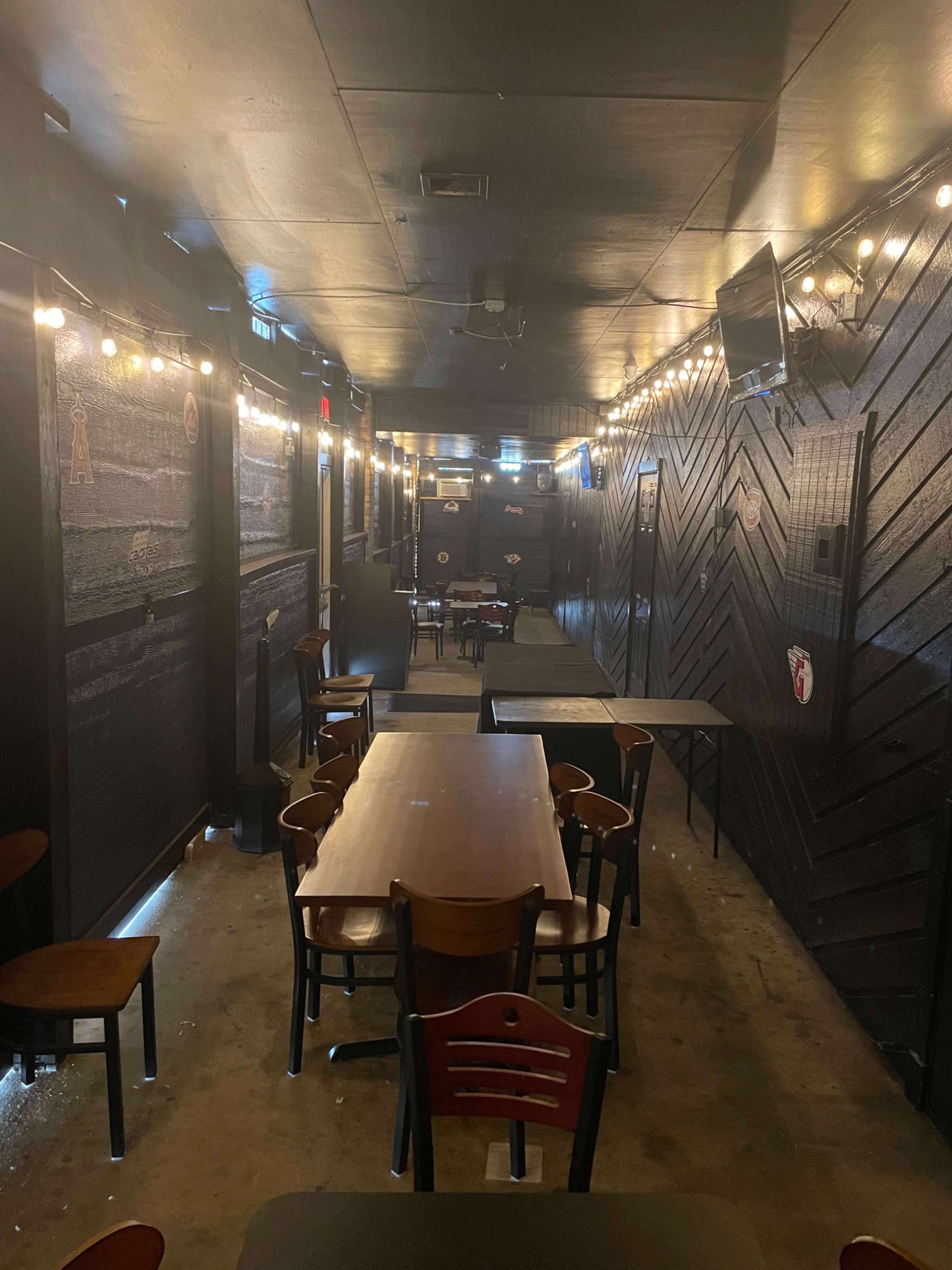 The image shows a dimly lit hallway in a restaurant or bar with multiple tables and string lights along the walls.
