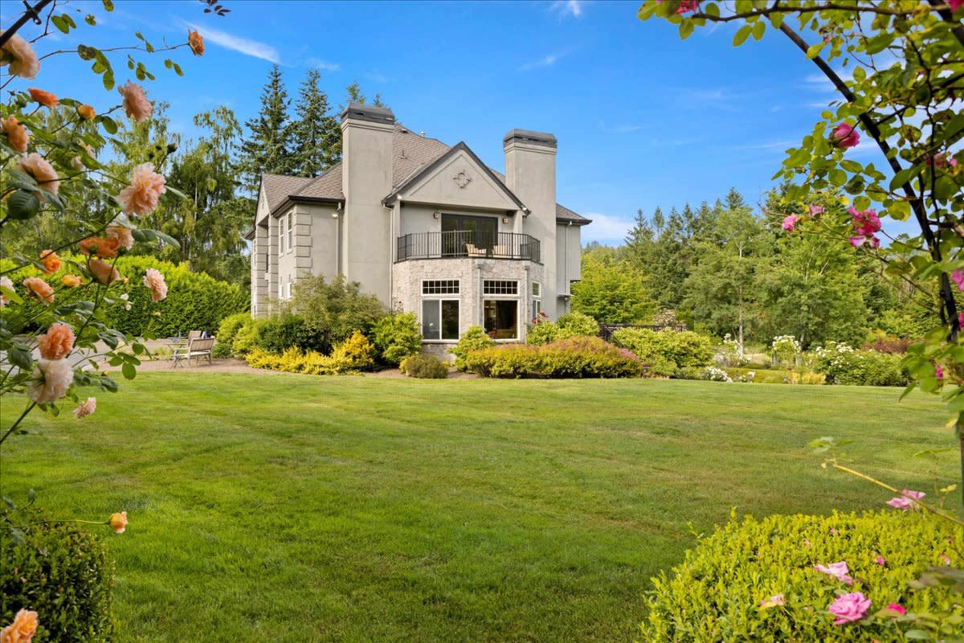 A large, modern house with a balanced design sits amidst well-maintained gardens and lush greenery.