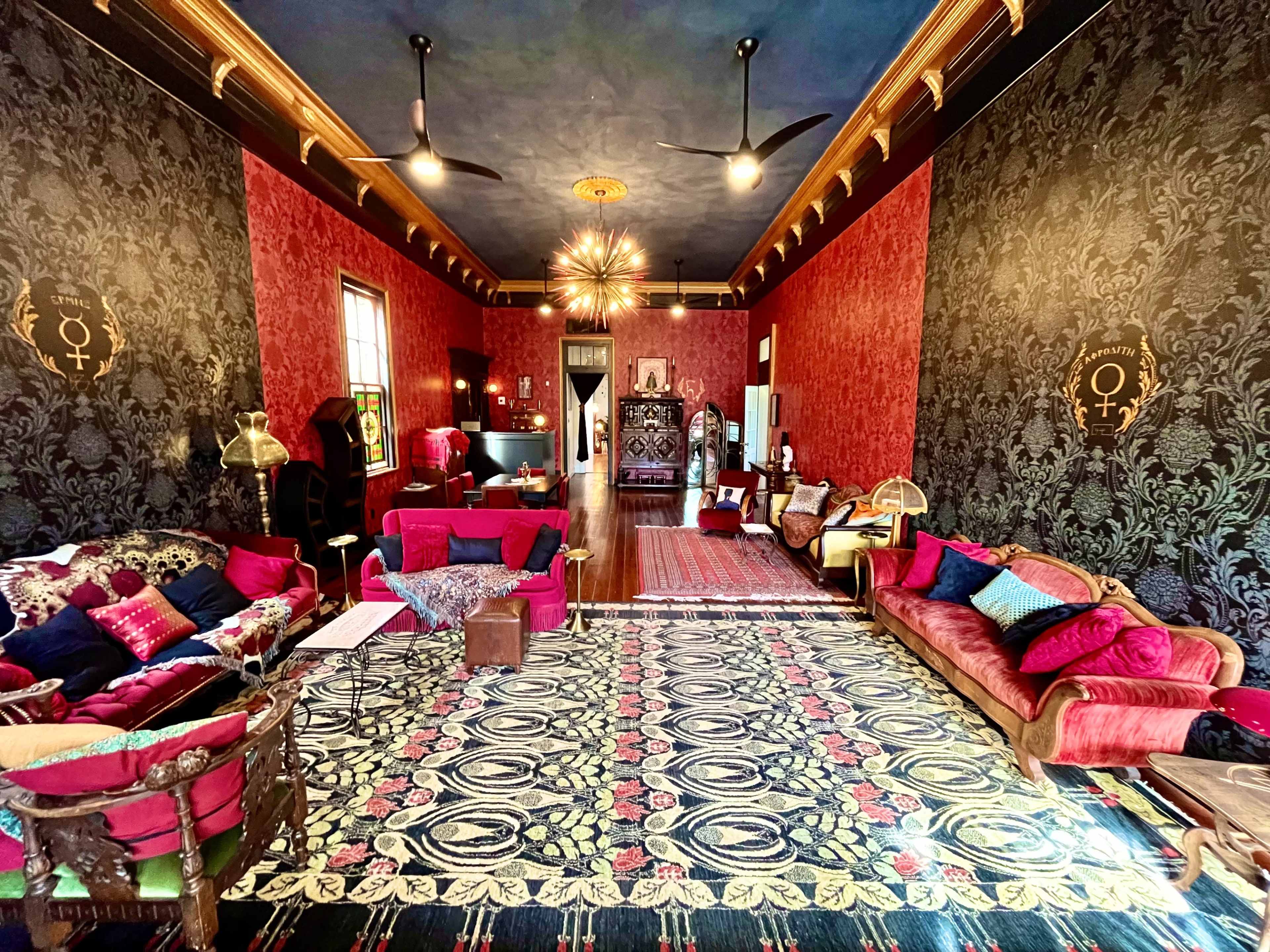 A spacious room with ornate wallpaper, red seating arrangements, and decorative lighting fixtures.