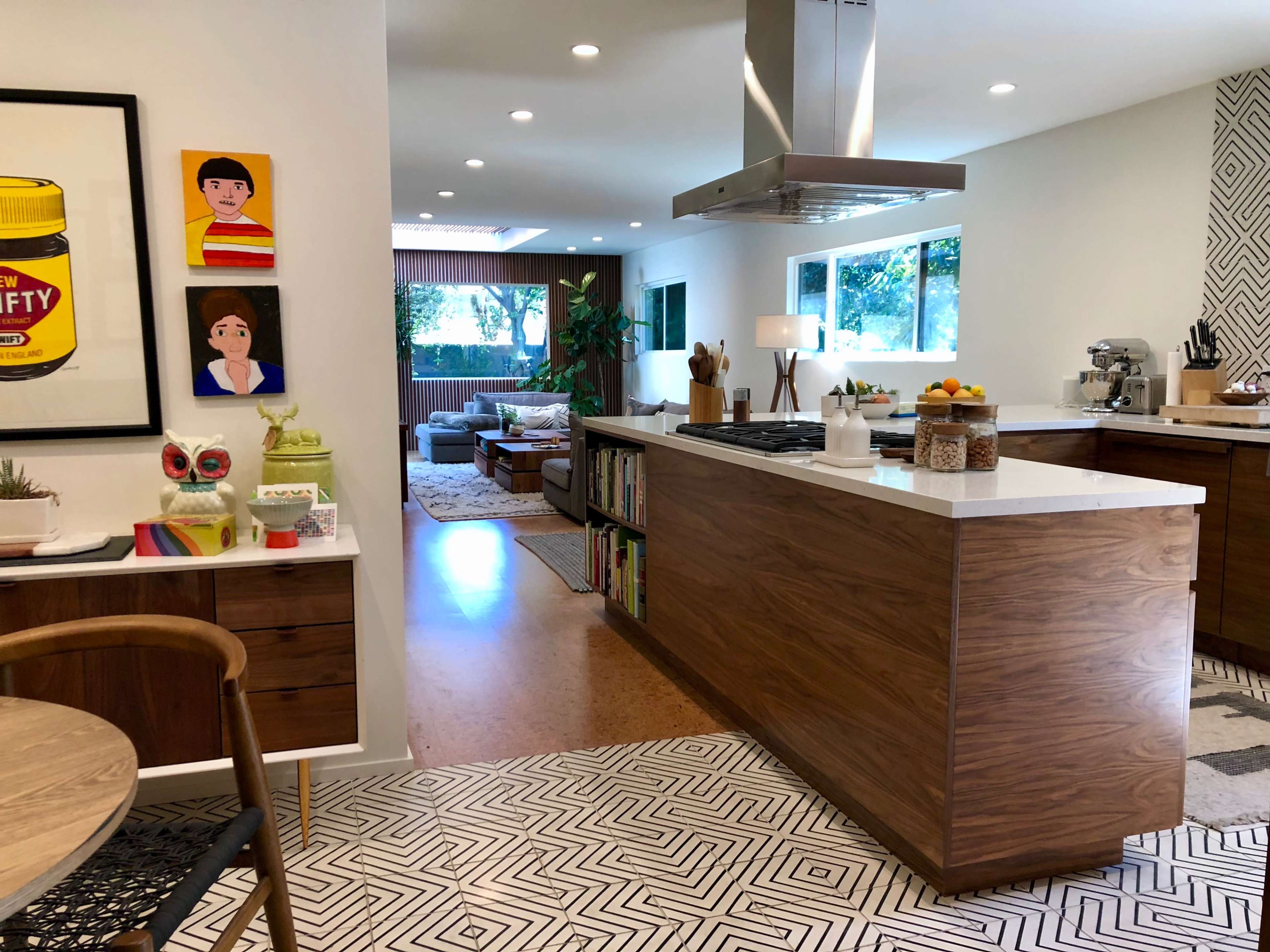 The image features a modern kitchen with an island, hardwood cabinets, and an open layout connecting to a living area.