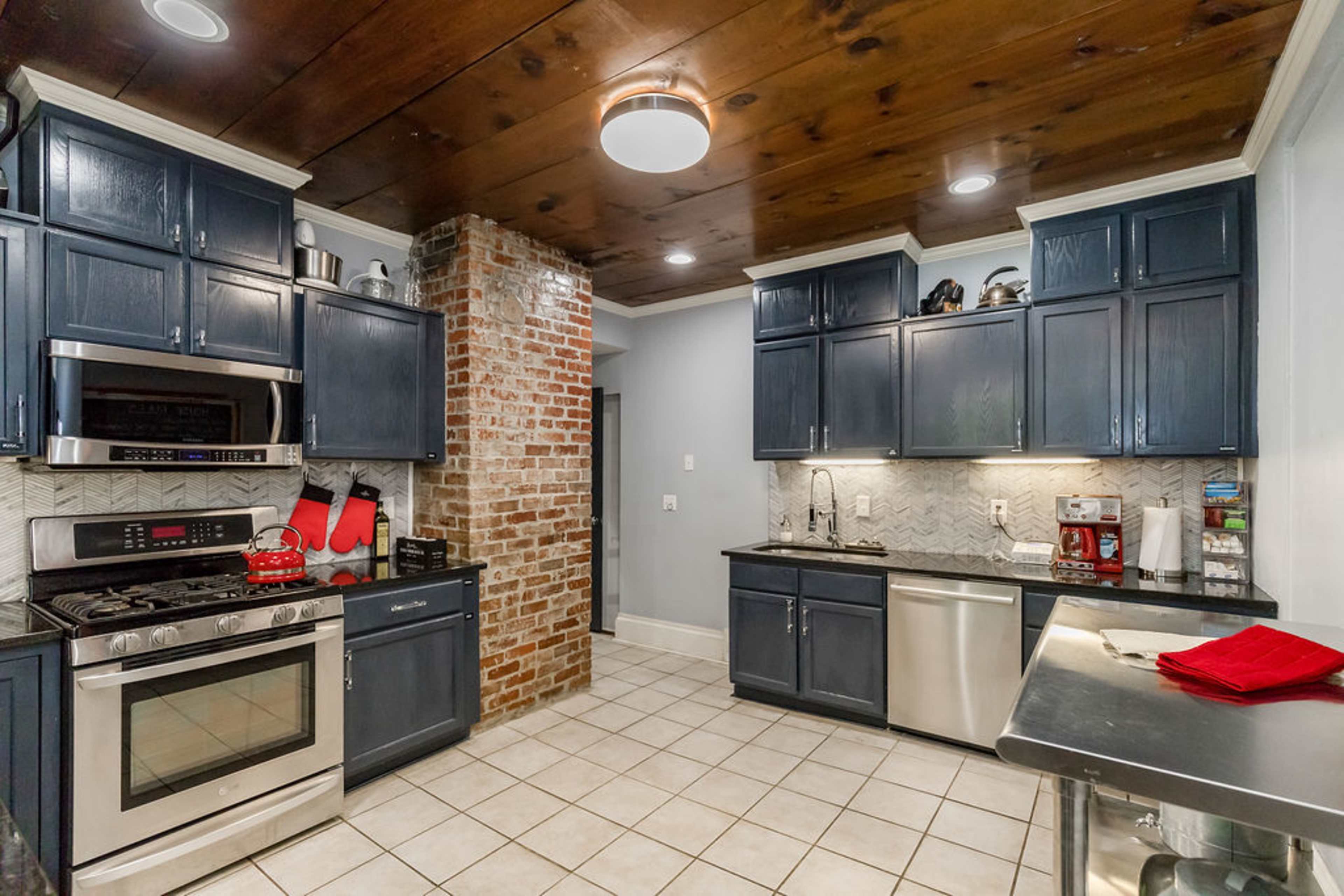 A modern kitchen with dark blue cabinets, stainless steel appliances, and a brick accent wall.