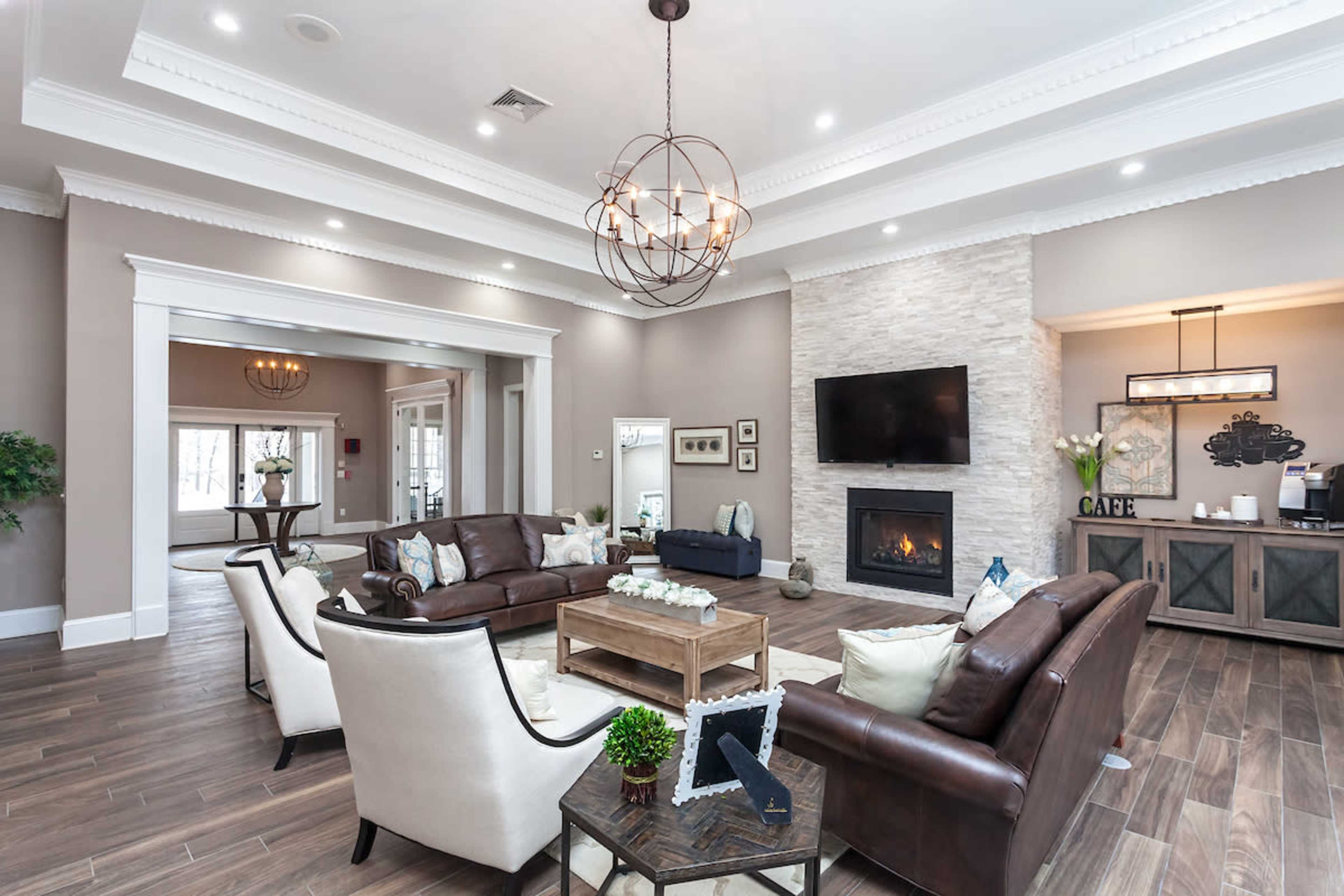 The image shows a spacious living room featuring a combination of leather and upholstered furniture, a stone accent wall with a mounted television, and a modern chandelier.