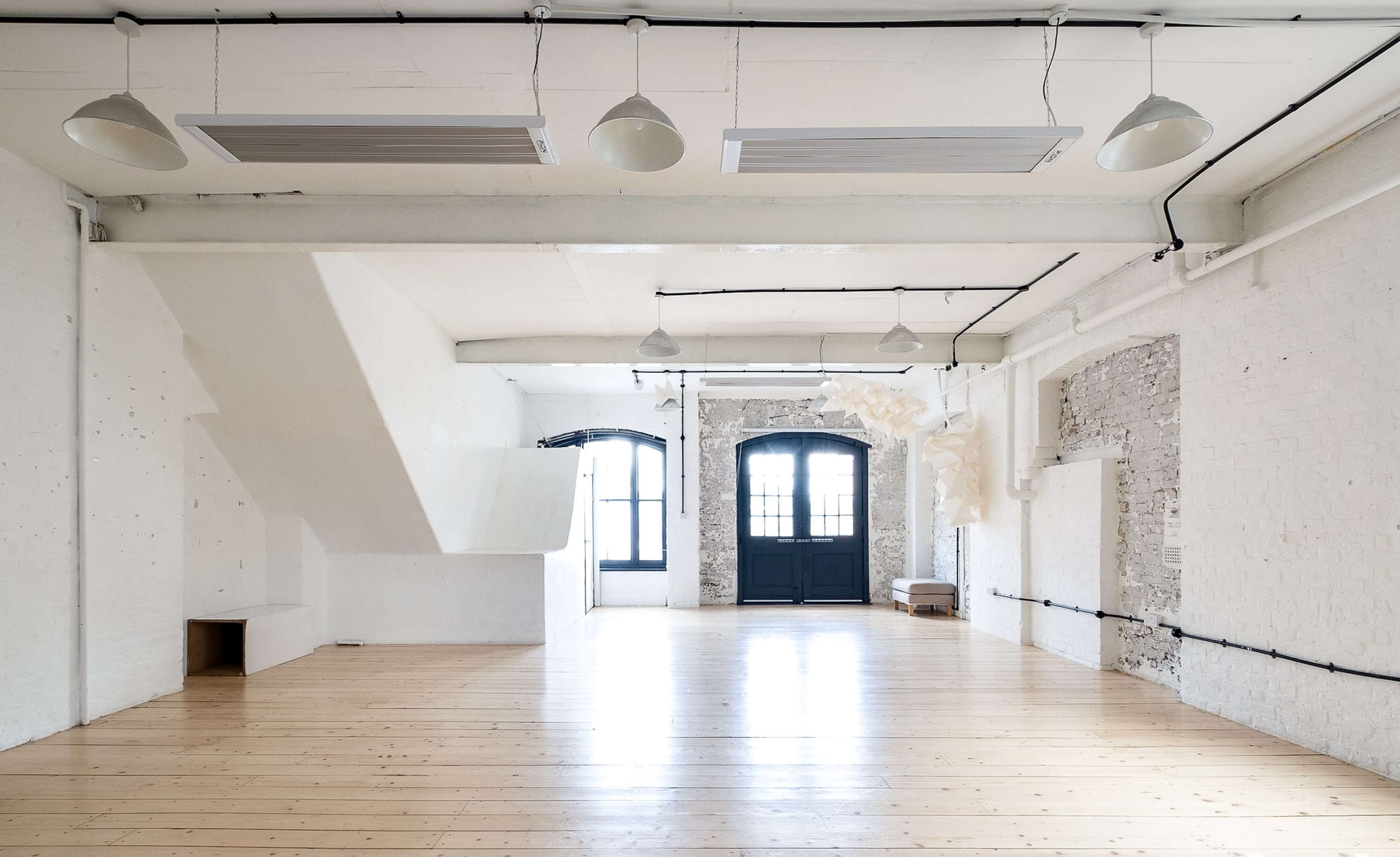 A spacious, light-filled room with wooden flooring, white walls, and large windows.