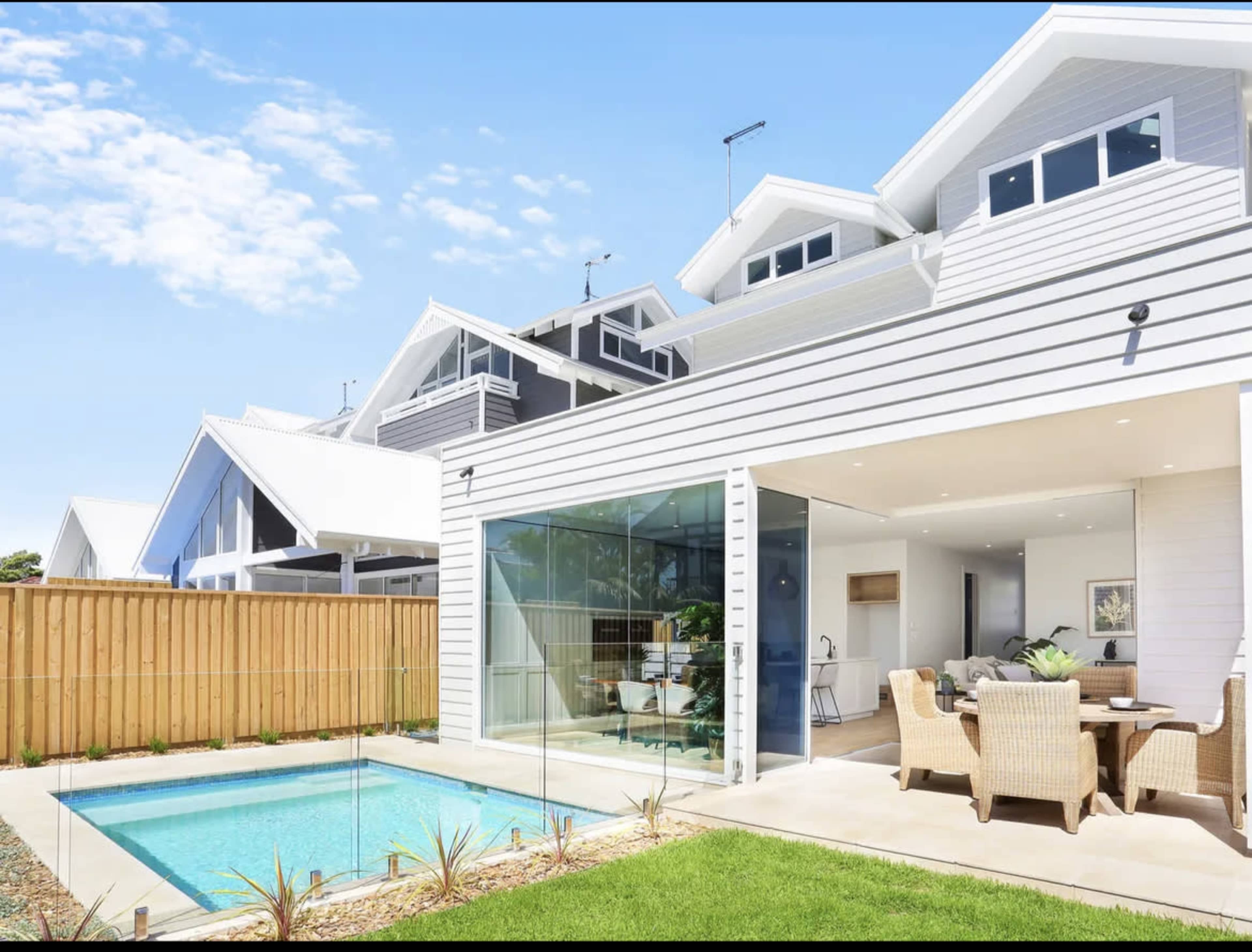 A modern two-story house with a glass wall opening to a small pool area and a patio with outdoor seating.