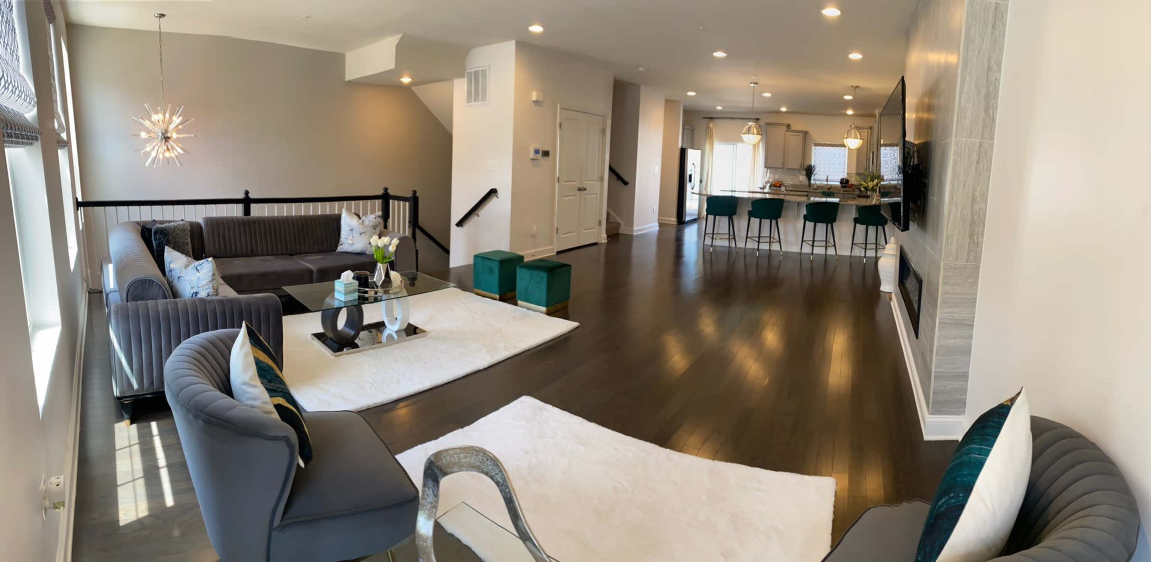 A modern, open-concept living space featuring a lounge area with gray sofas and a glass coffee table, leading to a dining and kitchen area with bar seating.