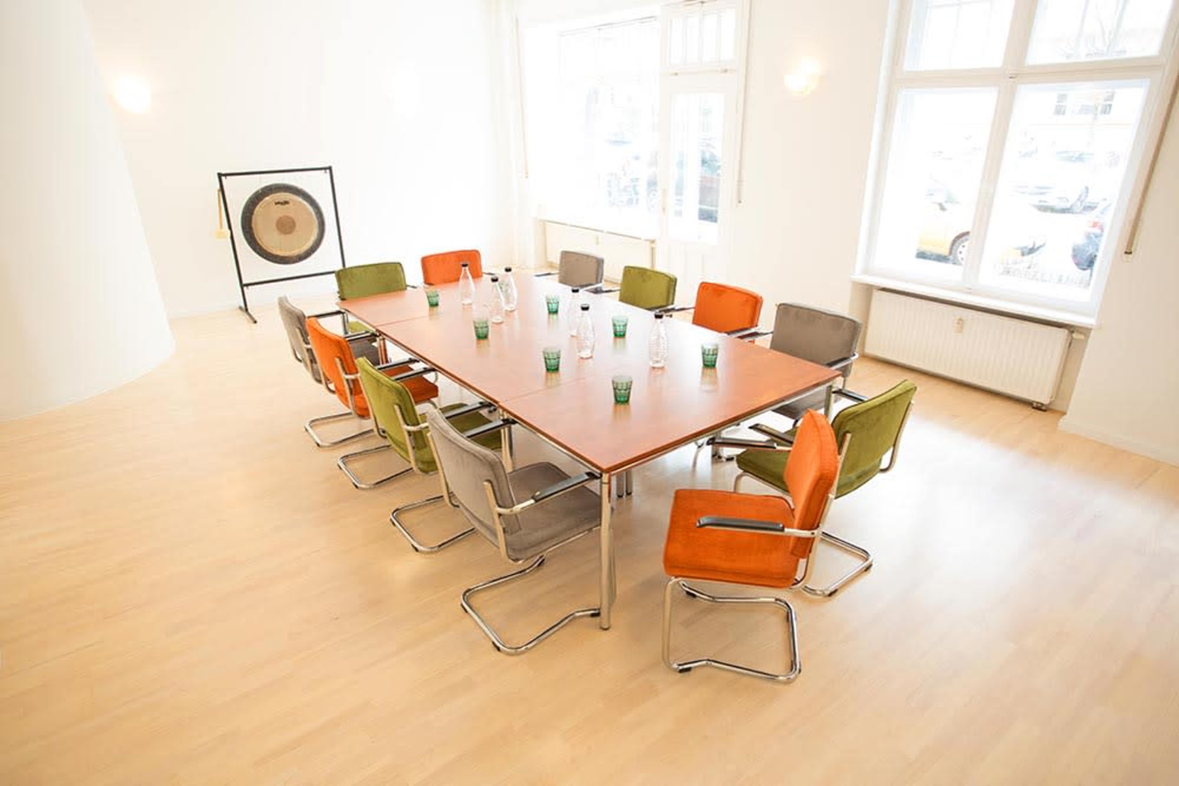 A spacious meeting room features a large rectangular table surrounded by colorful chairs and water bottles.