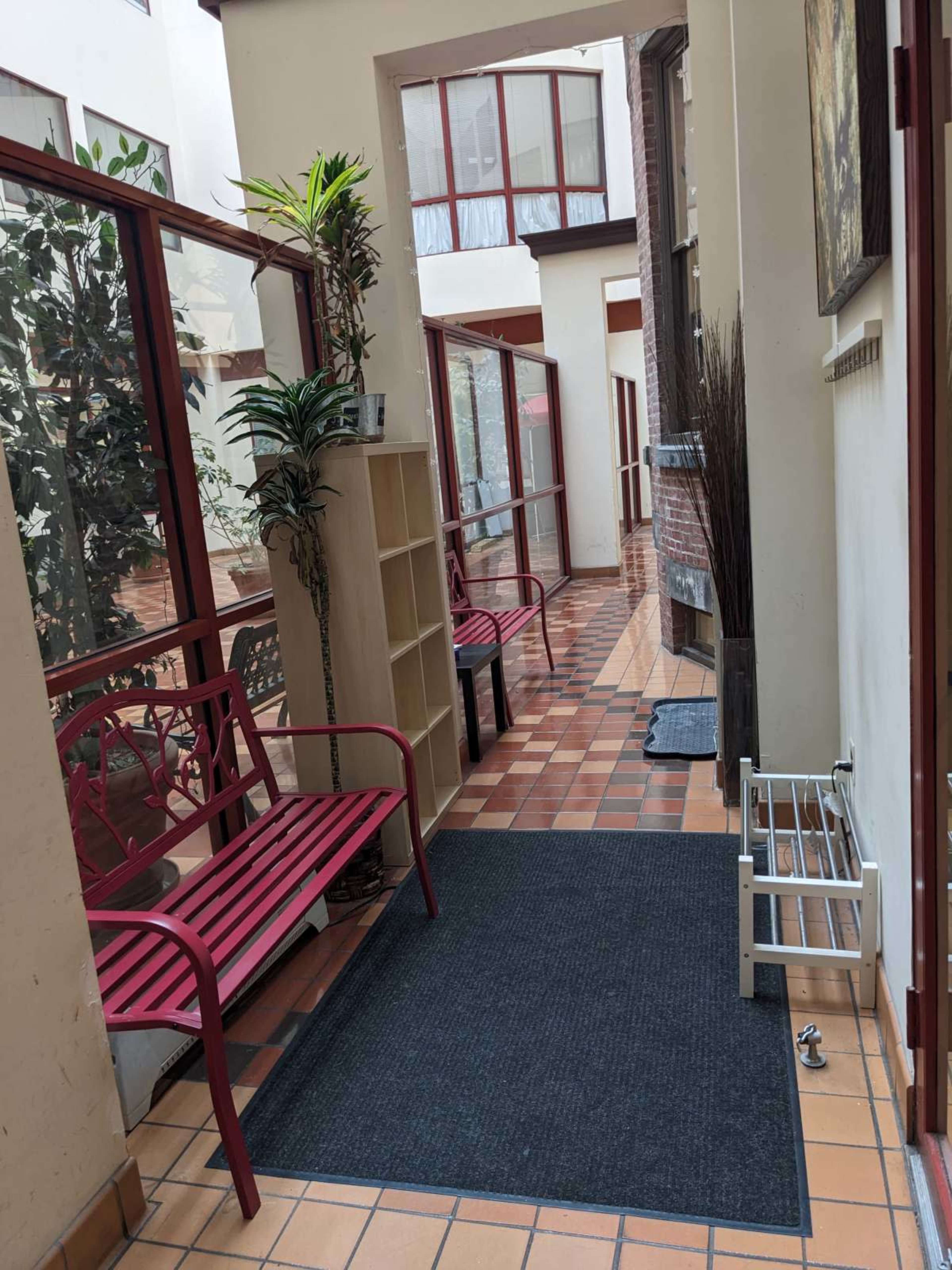 A narrow indoor corridor lined with benches, plants, and tiled flooring.