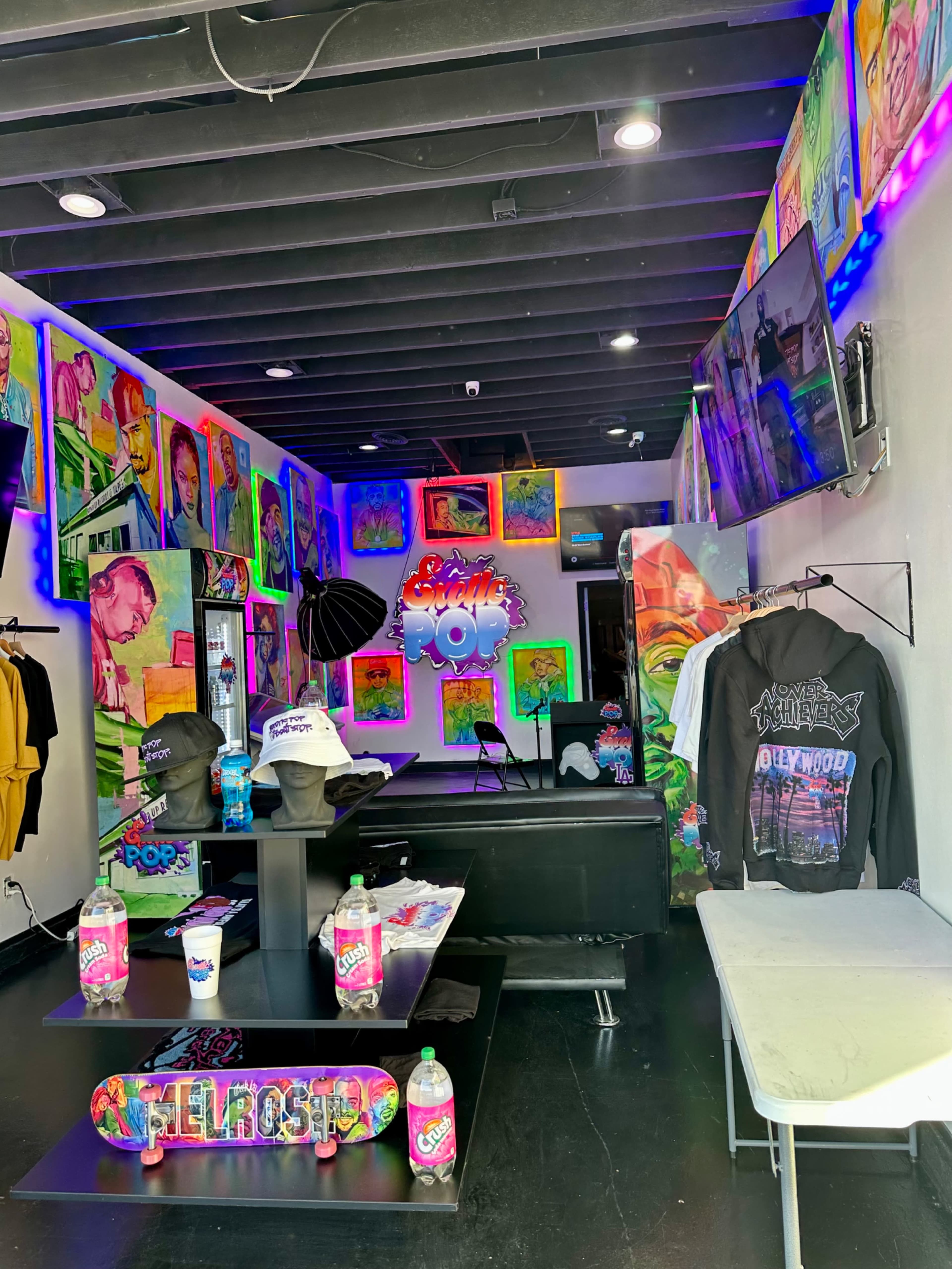 The image shows a colorful retail space decorated with vibrant artwork featuring various portraits, along with clothing and merchandise displayed on racks and tables.