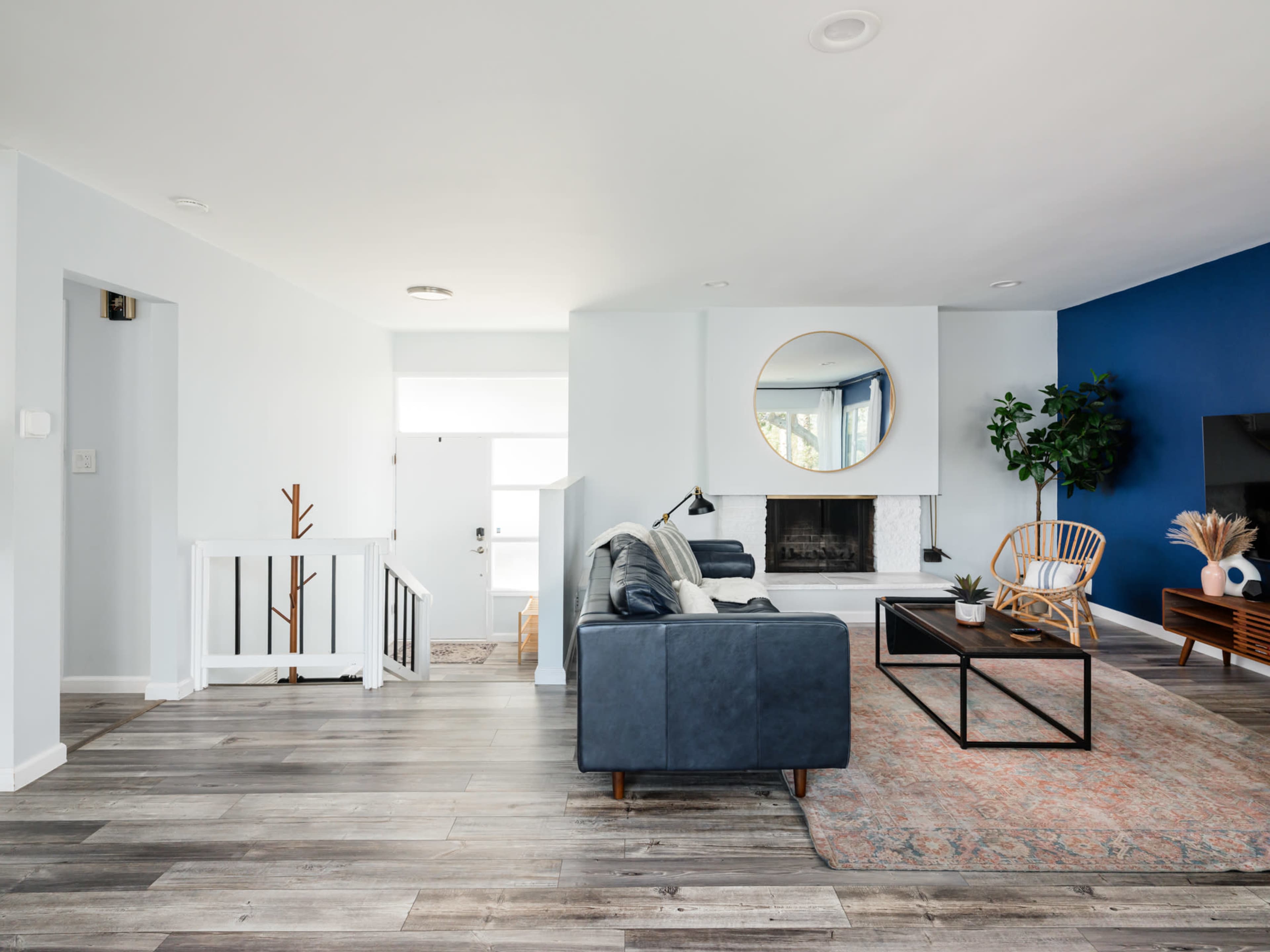 A modern living room features a blue accent wall, a fireplace, a round mirror, and a combination of seating and decorative elements.