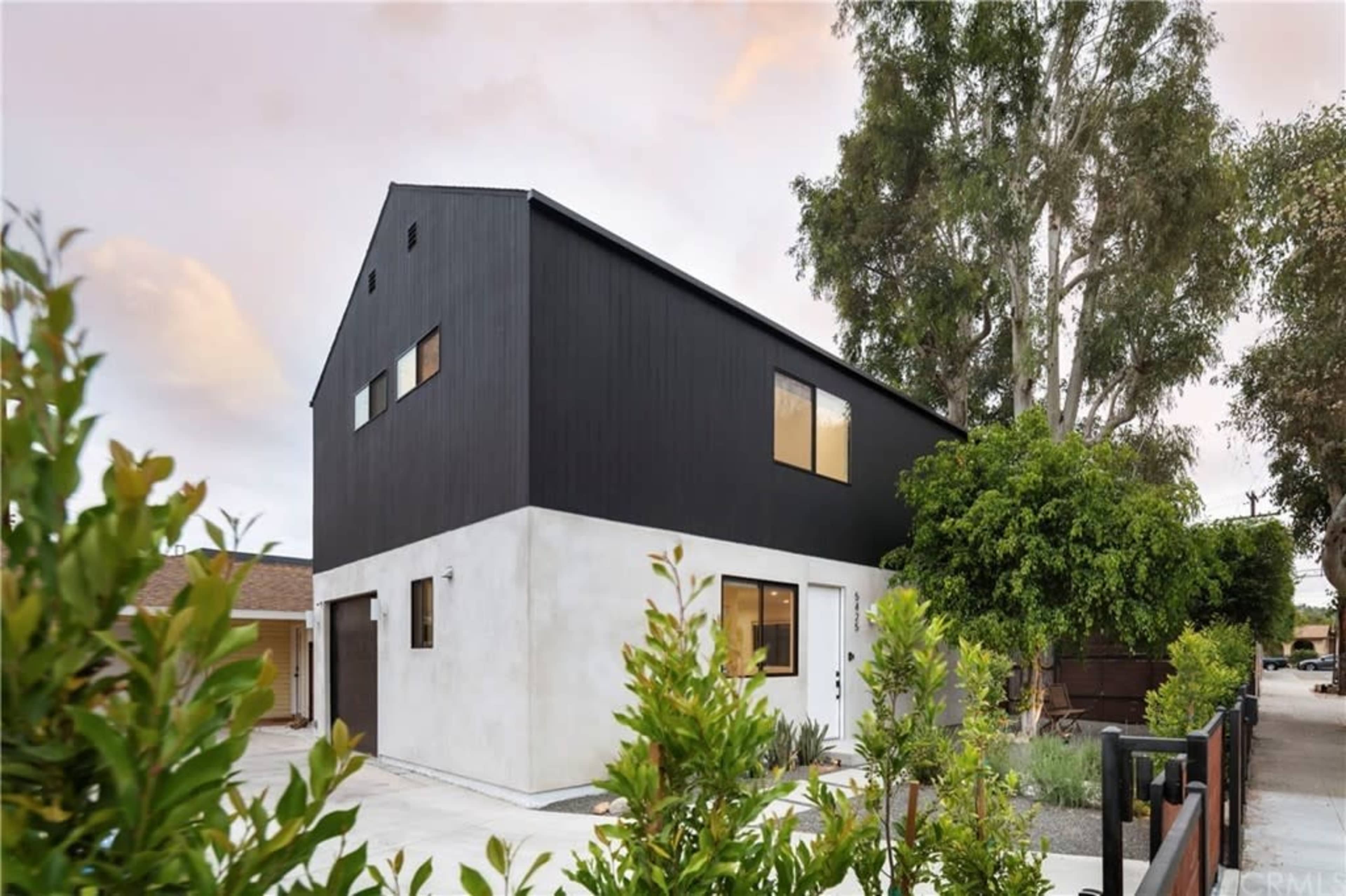 A modern two-story house with a black and white exterior, surrounded by greenery and a concrete driveway.